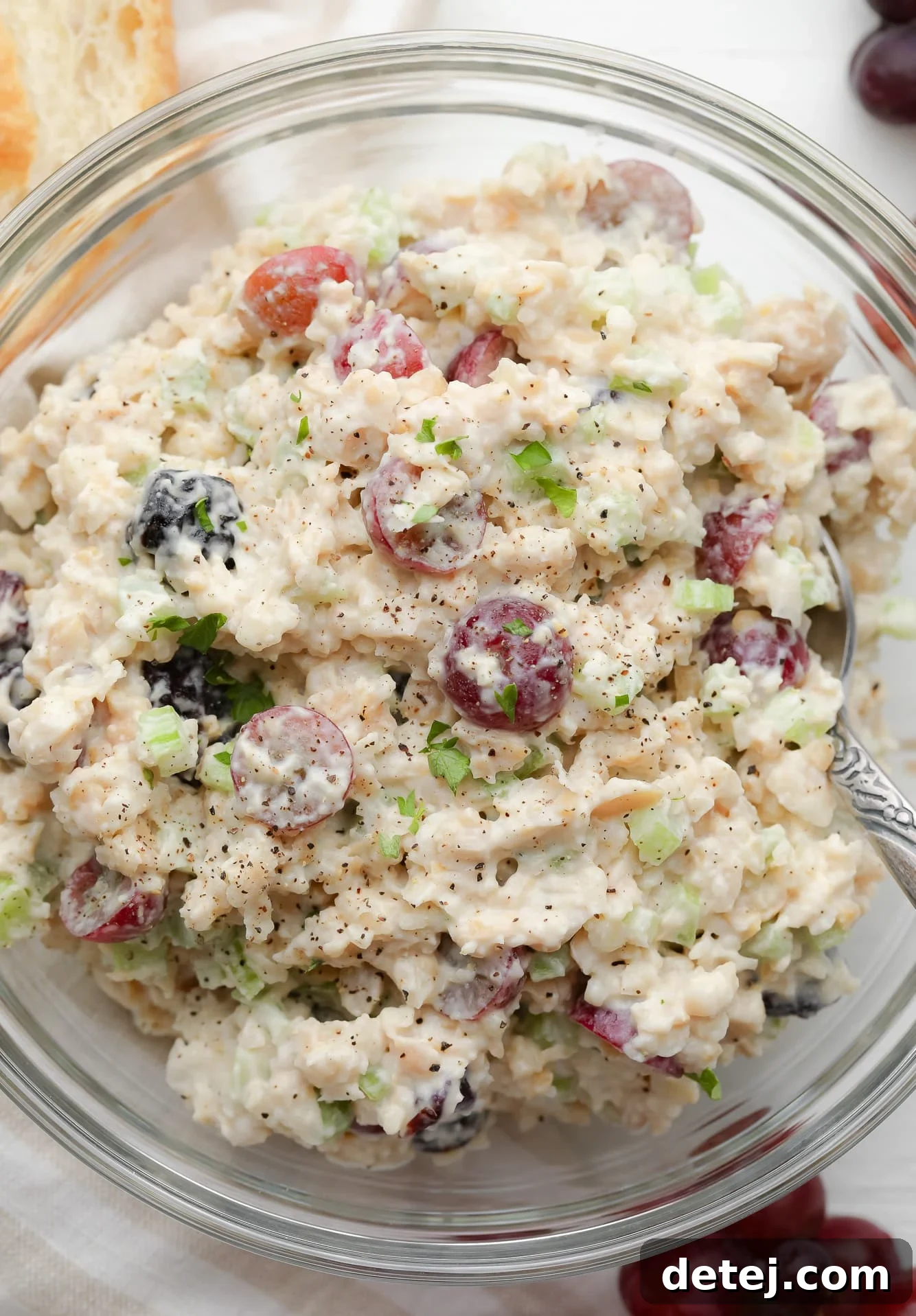 using a metal spoon to stir the ingredients for vegan chicken salad together in a large glass bowl.