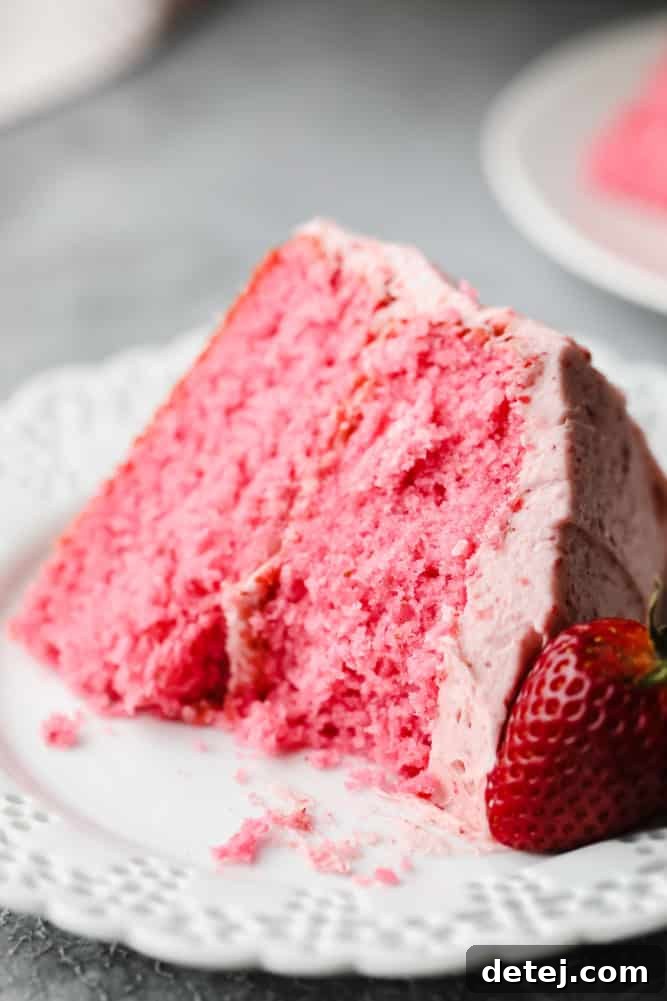 a bite taken from a piece of pink cake with strawberry on the side of the plate