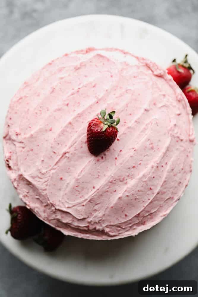 frosted pink cake with strawberries, on marble cake stand