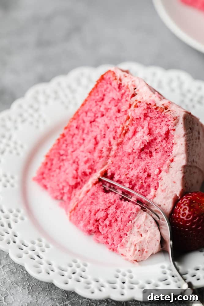 fork cutting into piece of vegan strawberry cake on white plate