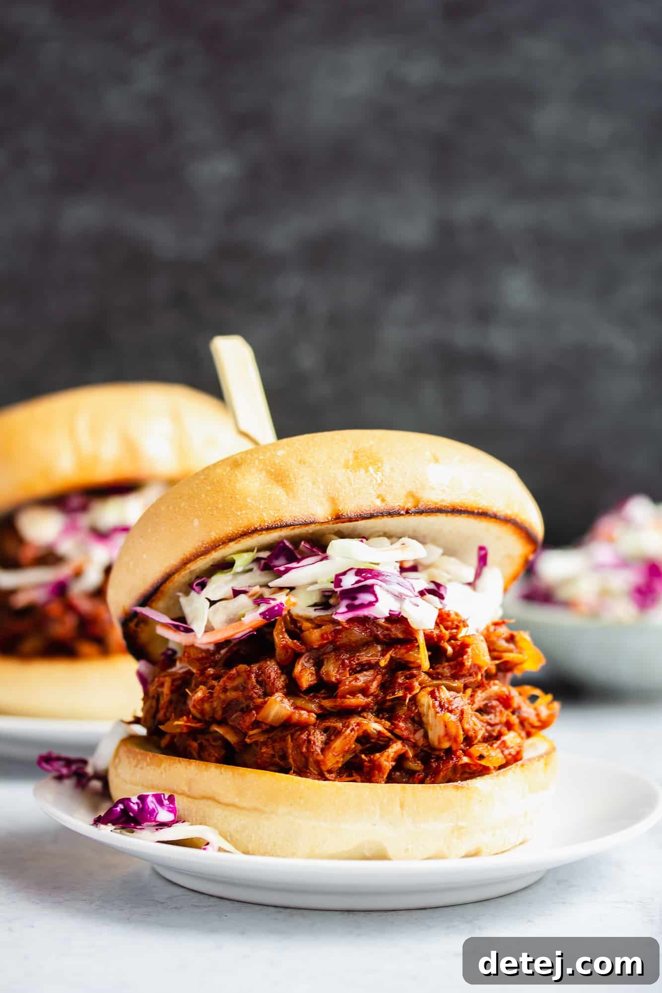 A perfectly assembled BBQ jackfruit pulled pork sandwich, generously topped with coleslaw, presented on a clean white plate.