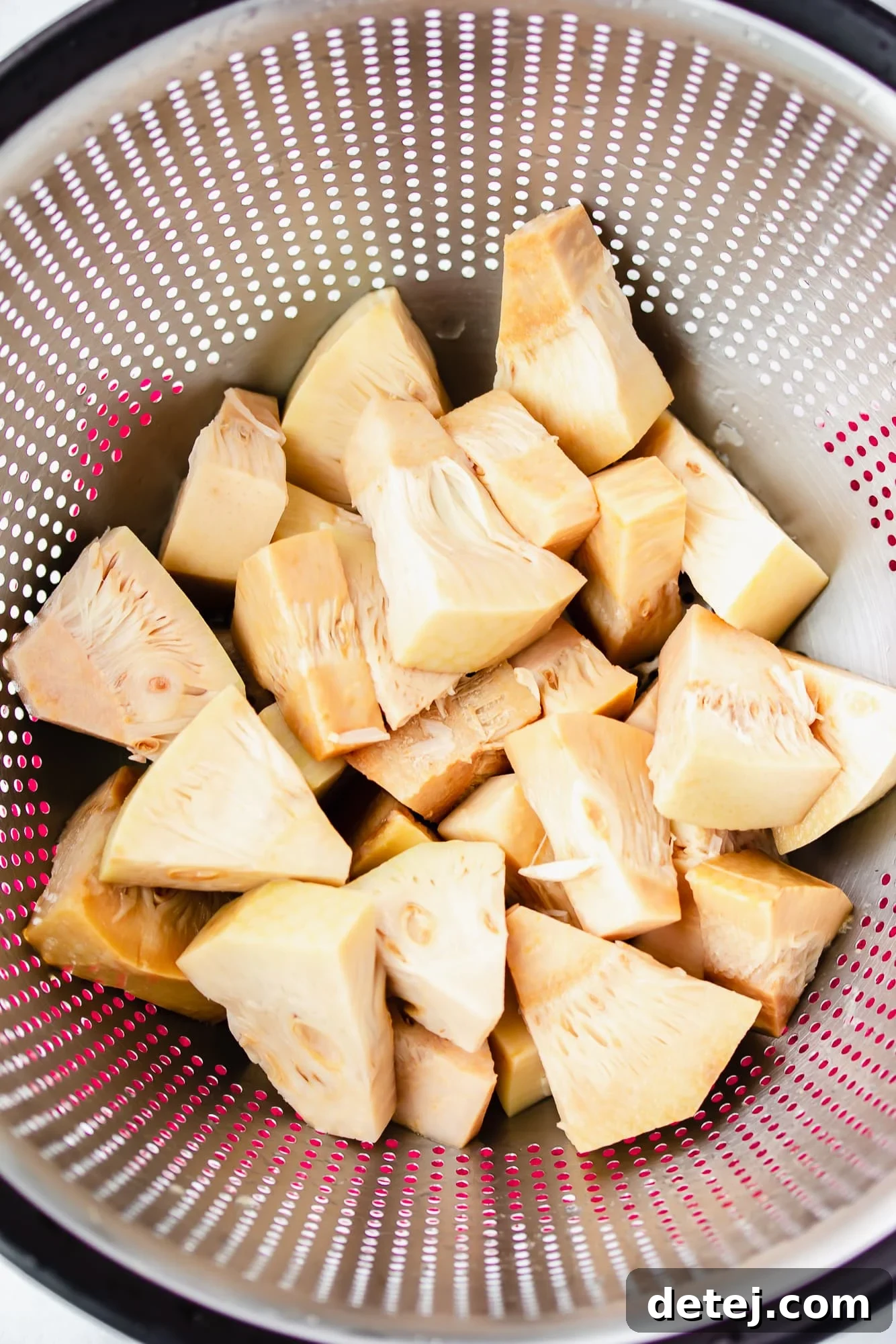 Young jackfruit pieces in a plastic strainer being rinsed under water, preparing them for cooking.