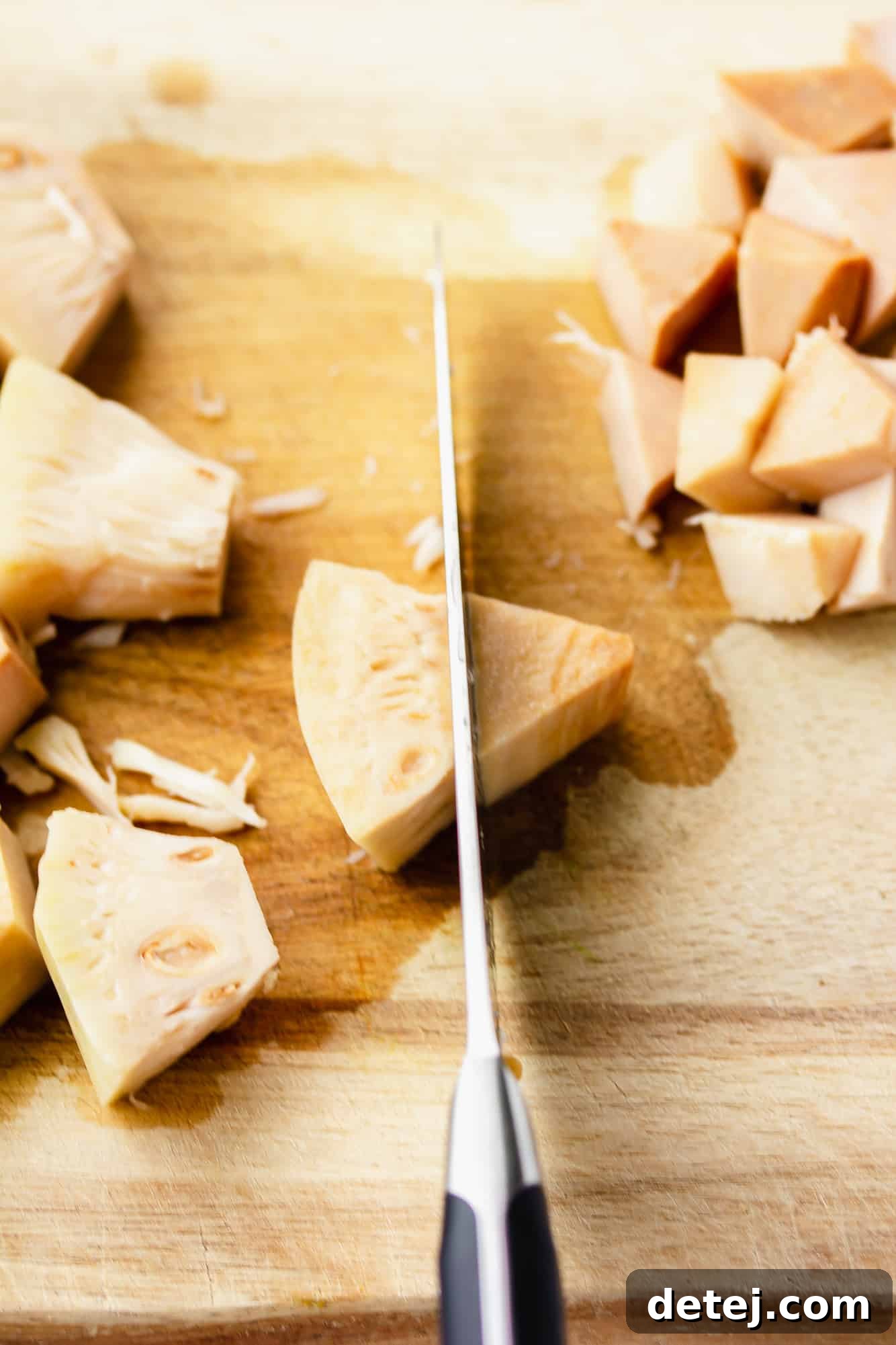 Using a knife to cut and trim young jackfruit on a wooden cutting board, preparing it for shredding.