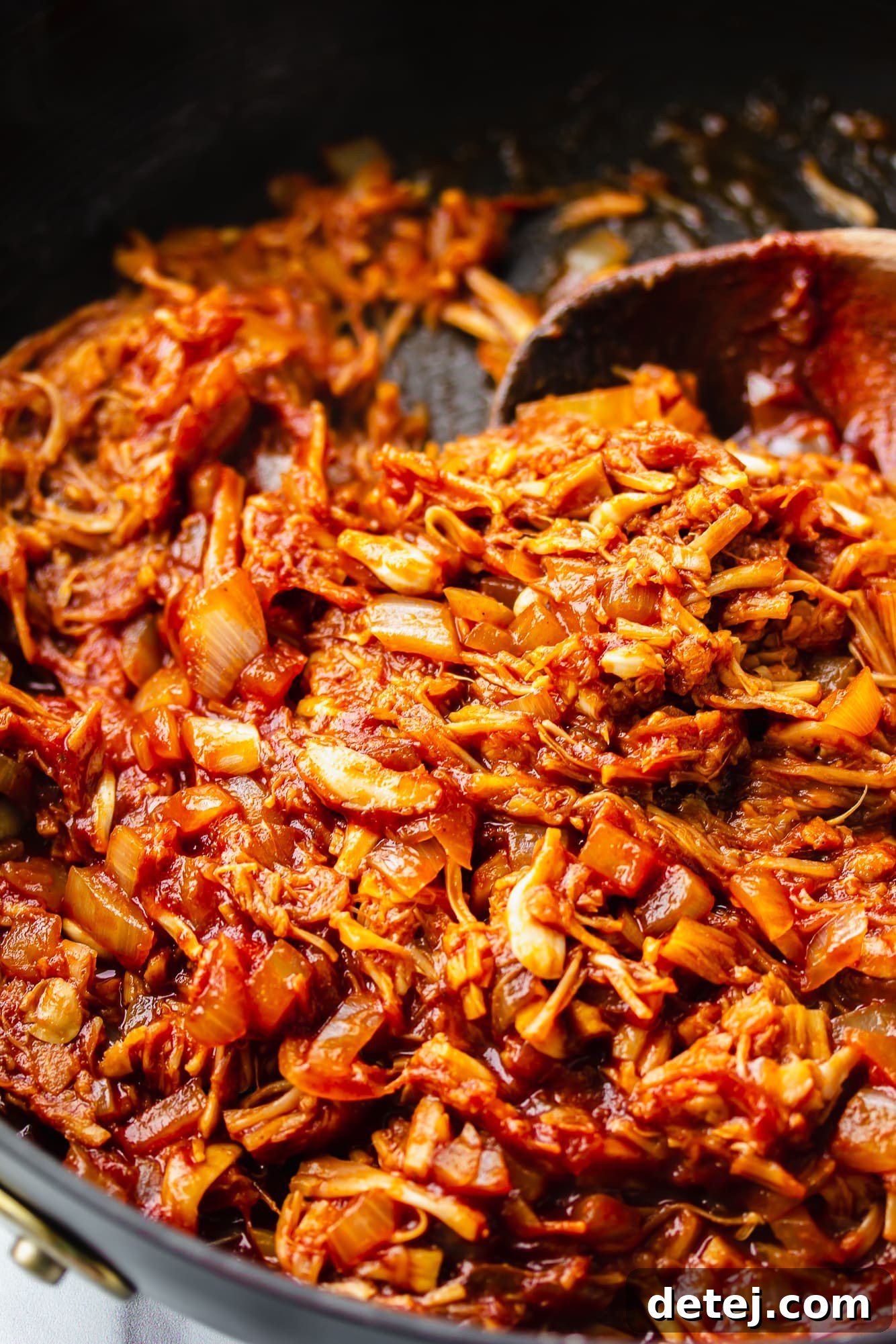 Stirring the finished BBQ jackfruit pulled pork with a wooden spoon in a skillet, showcasing its rich, caramelized texture.
