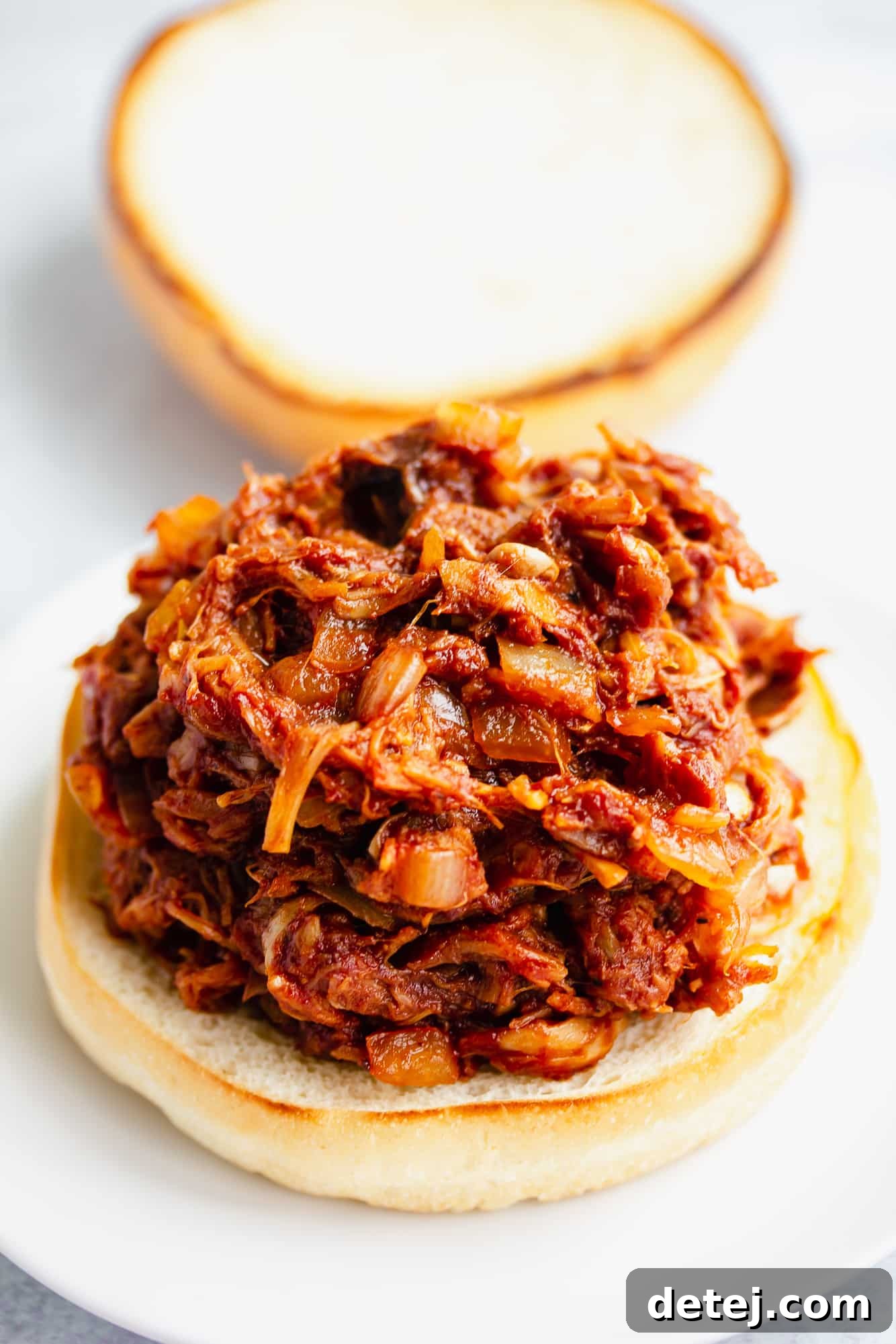 A close-up of BBQ jackfruit pulled pork nestled perfectly on a toasted hamburger bun, ready to be topped.