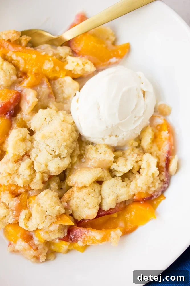 Homestyle Vegan Peach Cobbler 2 A bowl of freshly baked vegan peach cobbler topped with a scoop of vanilla ice cream, ready to be enjoyed.