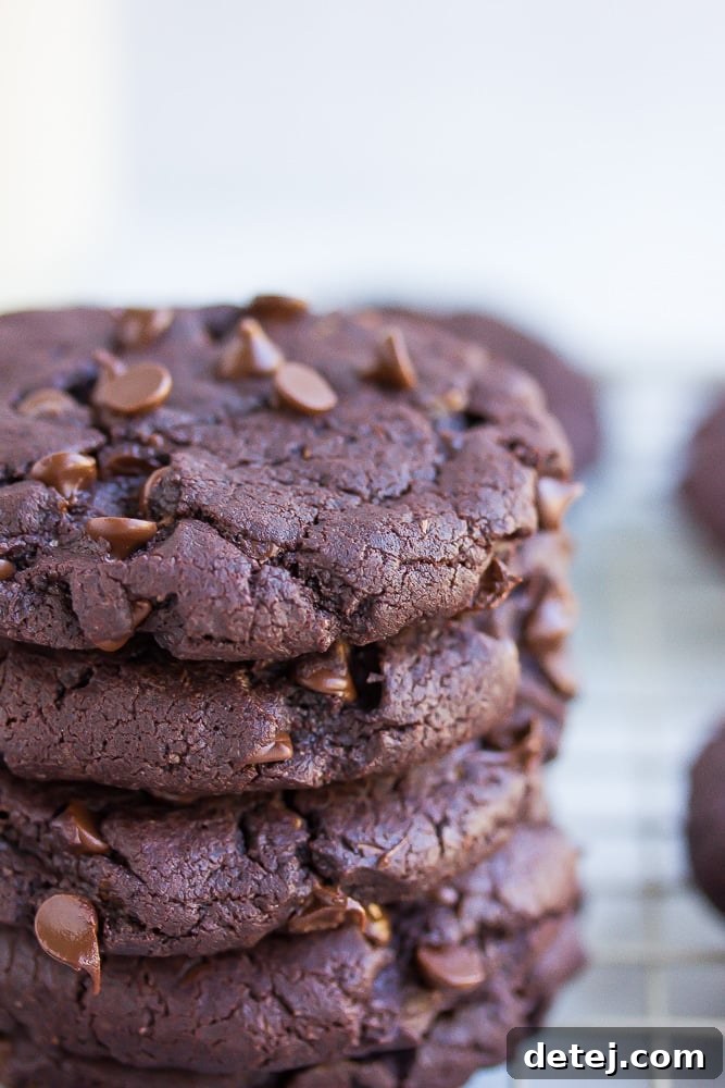 A close-up view of the side of a stack of vegan chocolate cookies, revealing their dense, fudgy texture and generous distribution of chocolate chips.