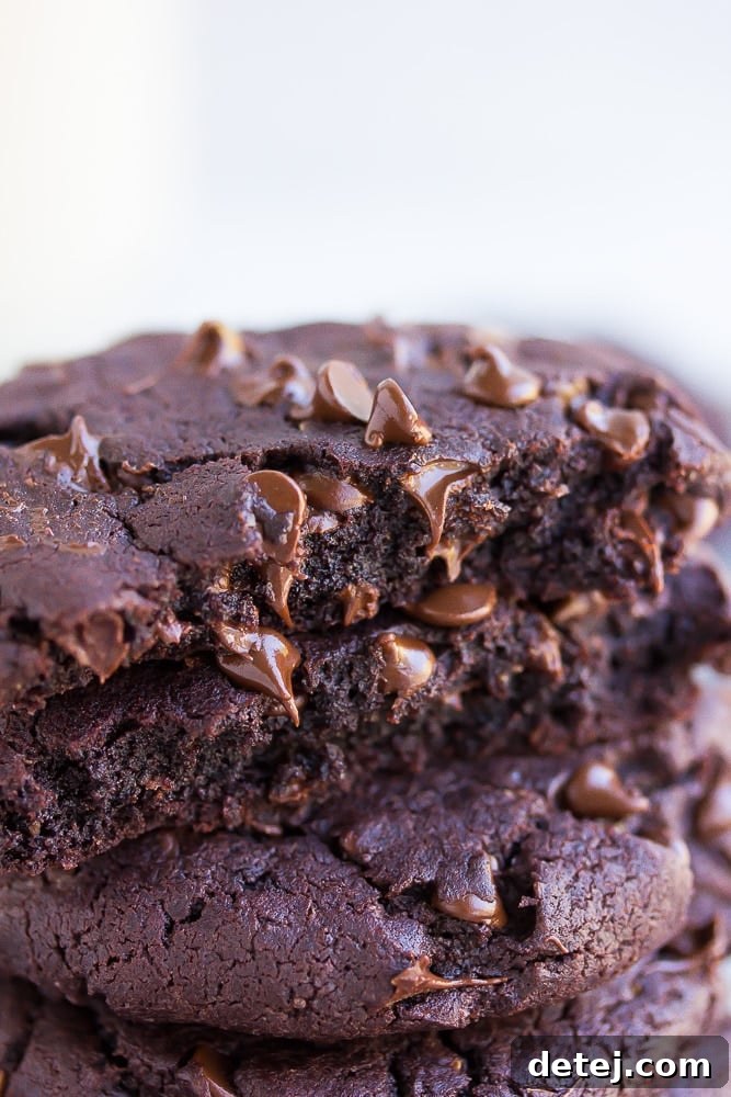 A close-up shot of a vegan chocolate cookie broken in half, showing its incredibly fudgy, dense interior and molten chocolate chips.