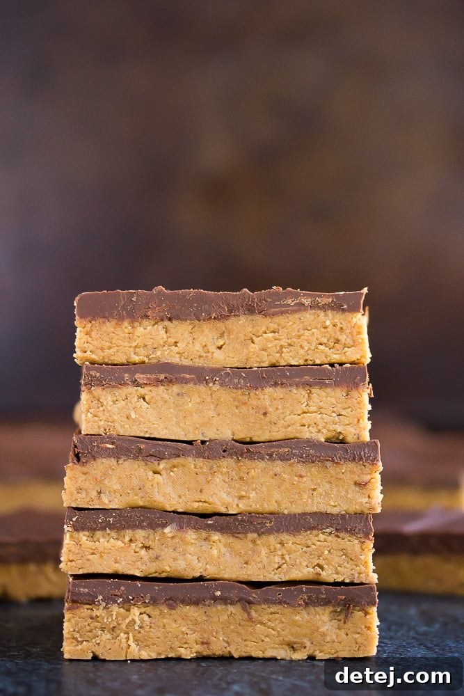 A stack of three rich Vegan Chocolate Peanut Butter Bars against a dark, moody background, highlighting their thick chocolate layer and creamy texture.