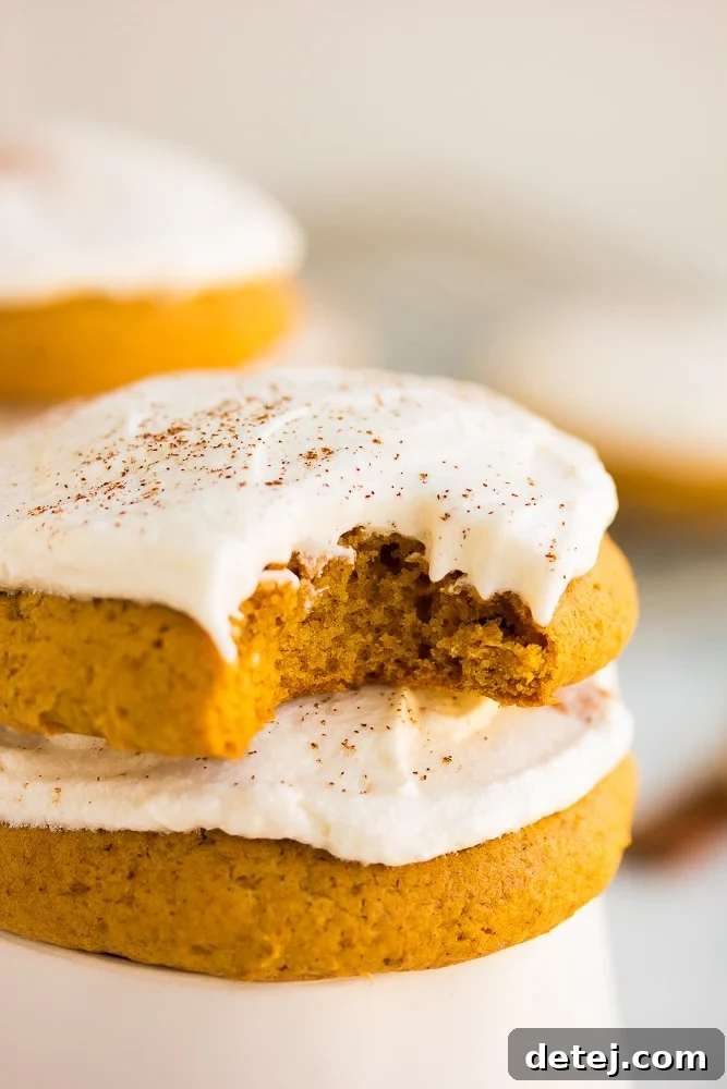 close up of a vegan pumpkin cookie with a bite taken out of one. Perfectly soft and frosted.