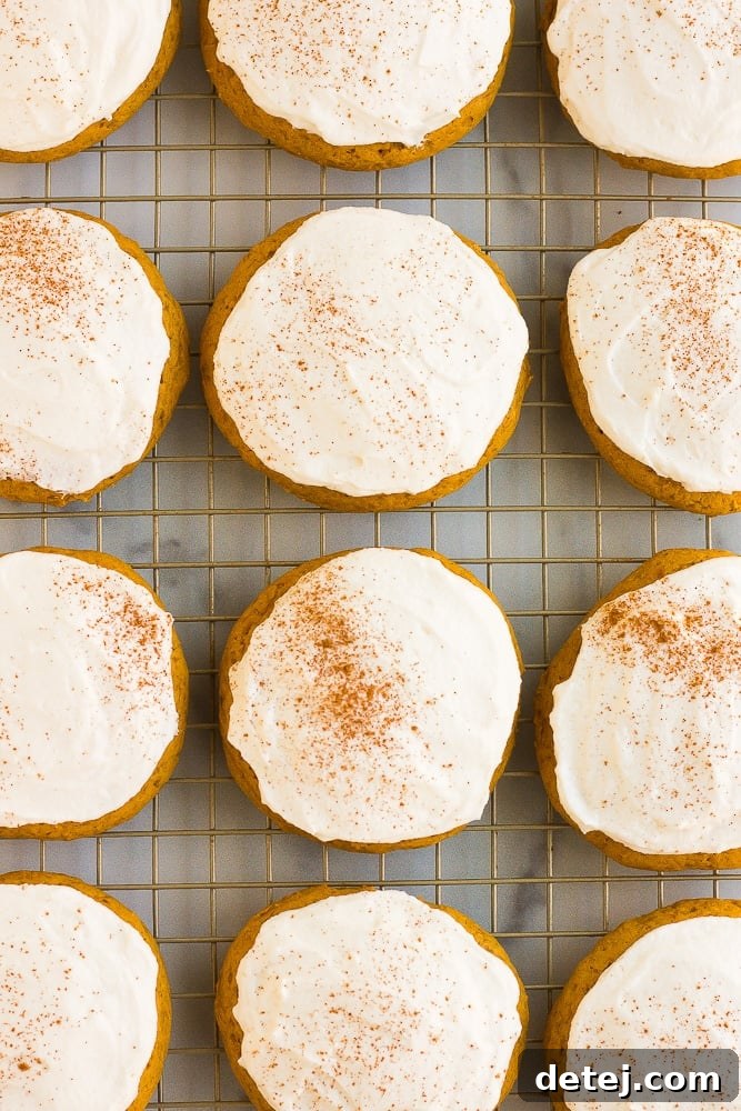lots of frosted vegan pumpkin cookies on a baking sheet, ready to be enjoyed.