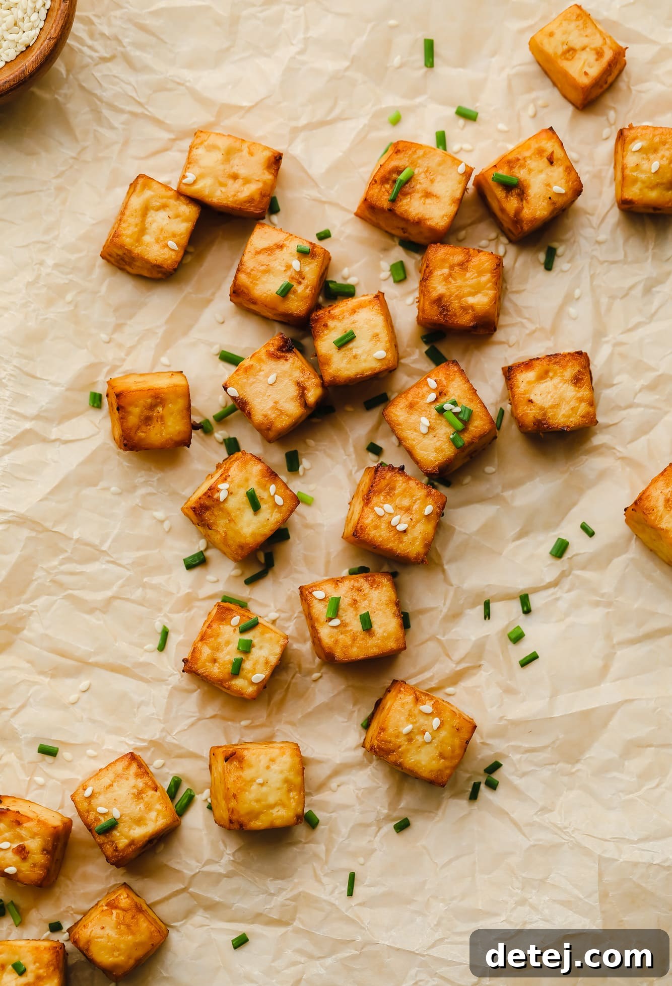 crispy air fryer tofu cubes garnished with sesame seeds and chives on a piece of parchment paper.
