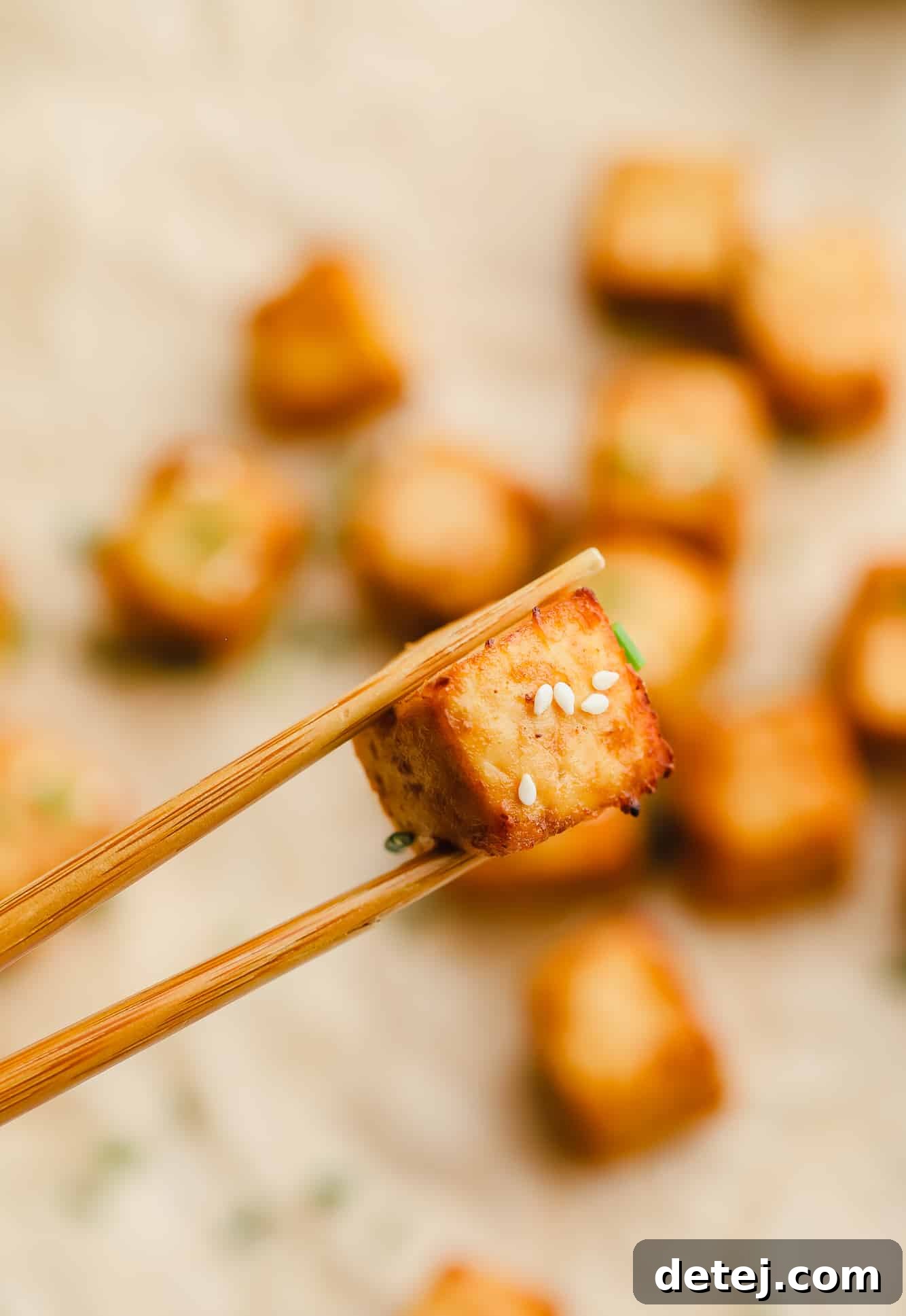 close up of an air fryer tofu cube being held up by wood chopsticks.