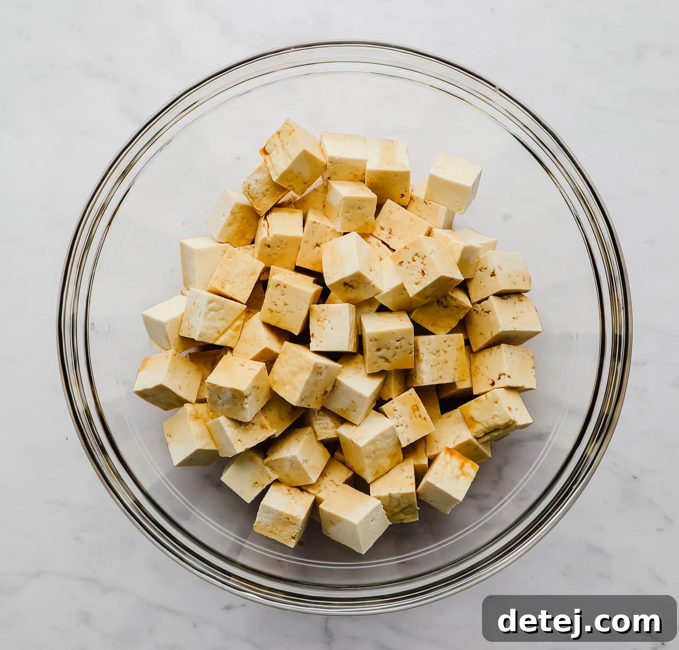 tofu cubes drizzled with soy sauce in a large glass bowl.