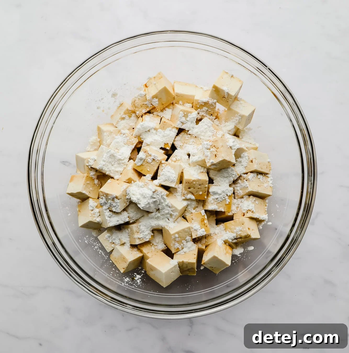 sprinkling cornstarch on top of tofu cubes in a large glass bowl.