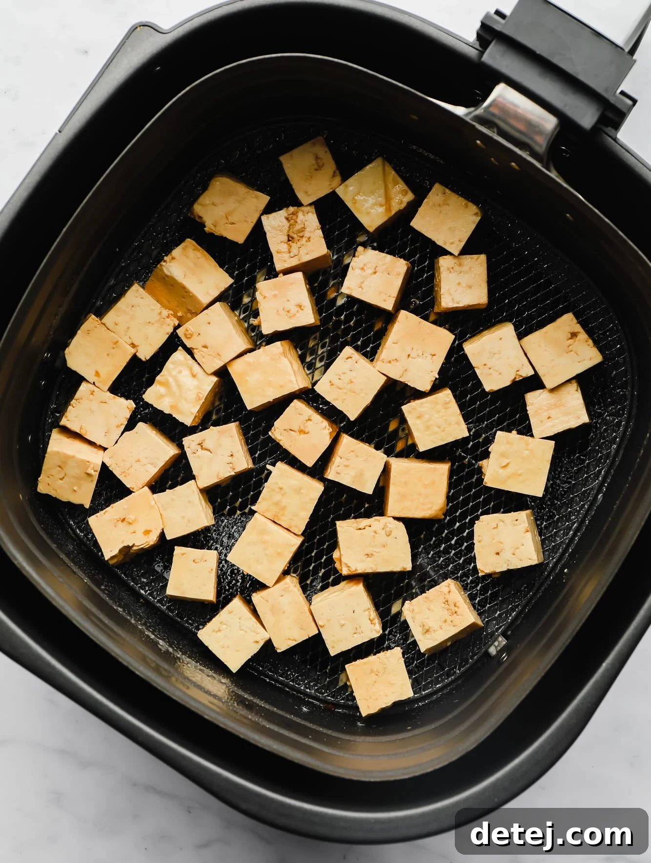 raw tofu cubes in an air fryer basket.