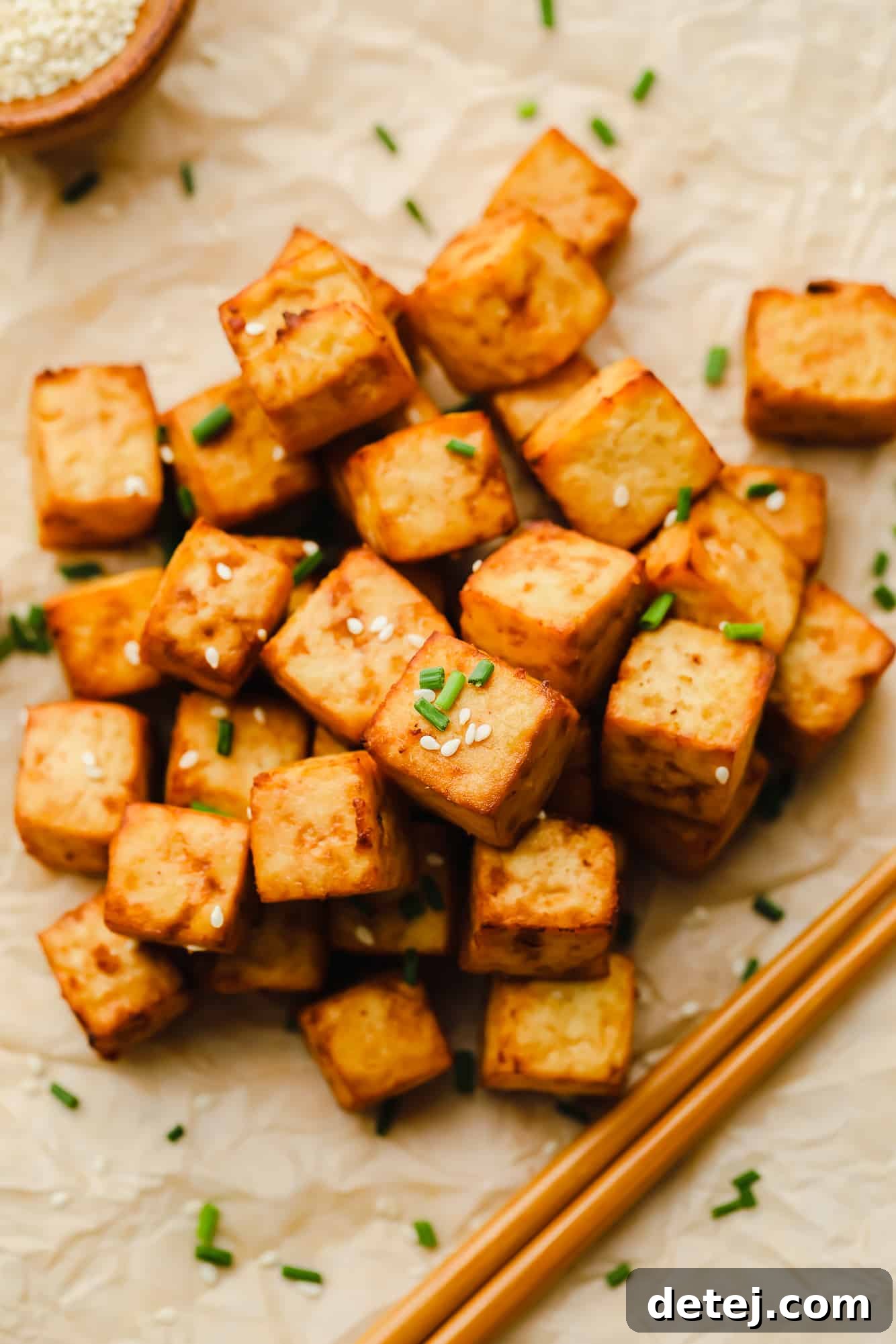 a pile of air fryer tofu garnished with sesame seeds and chives.