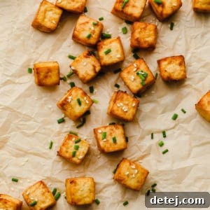close up of air fryer tofu on parchment paper garnished with sesame seeds and chives.