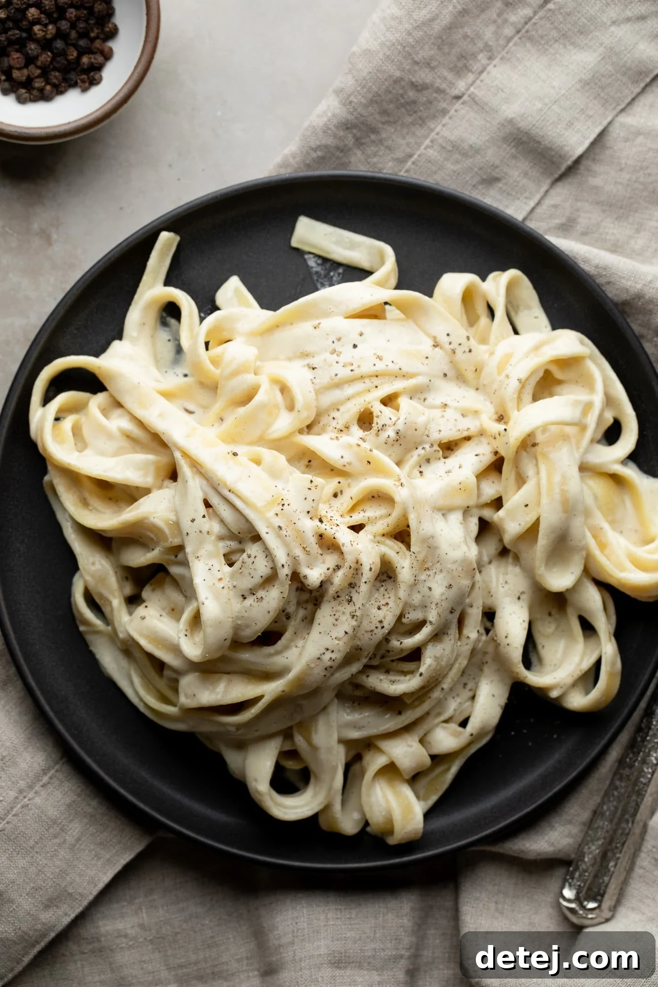 vegan alfredo with fettuccine on a black plate, grey background
