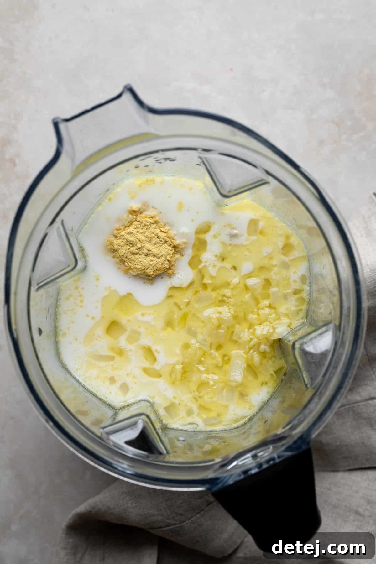 blender with what looks like milk, onions and nutritional yeast not yet blended