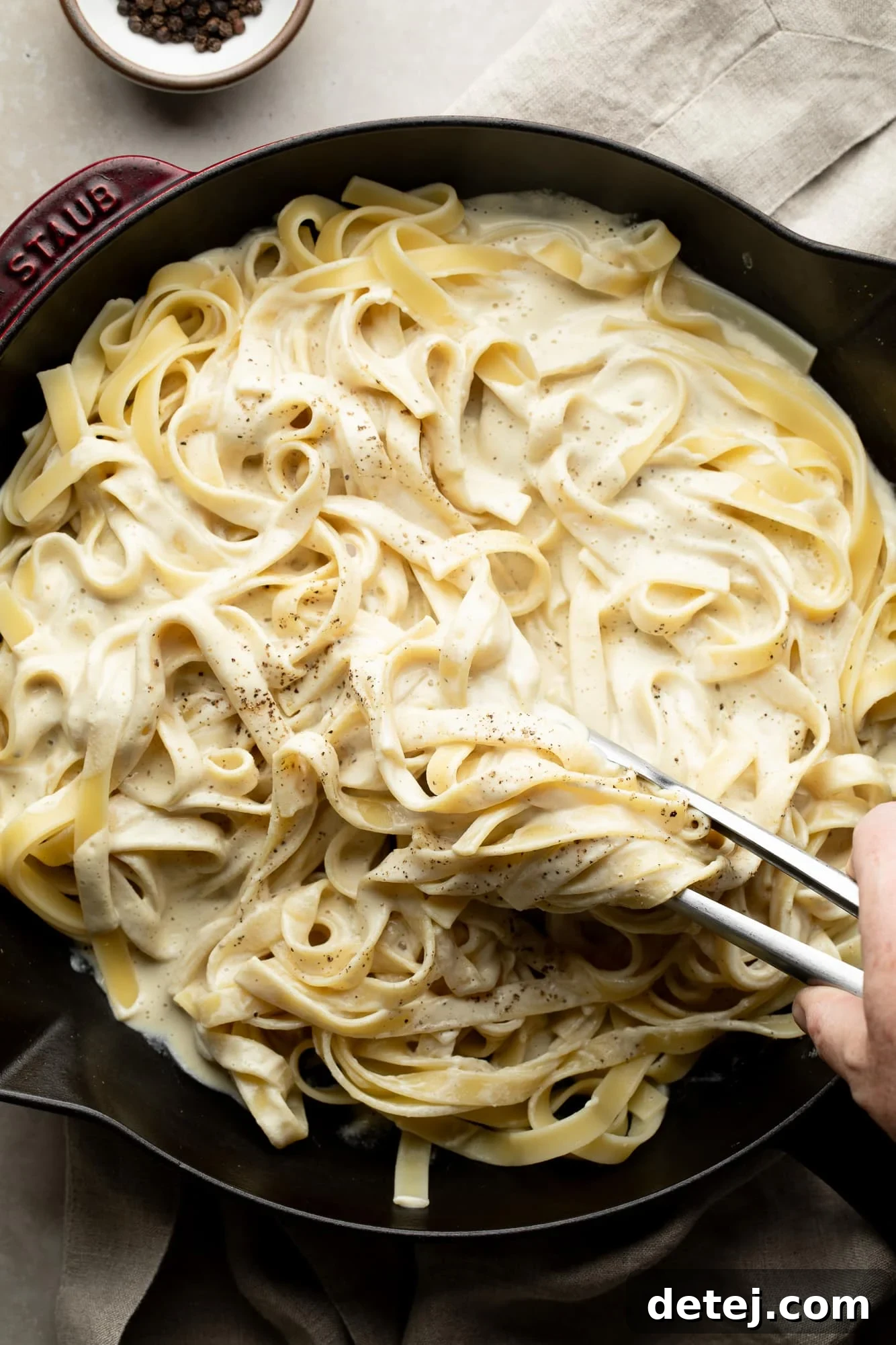 cast iron pan with fettuccine alfredo and tongs mixing it up with the sauce