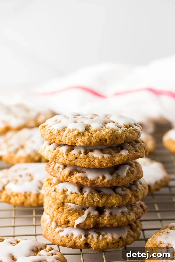 A beautifully stacked pile of iced vegan oatmeal cookies, with a red and white checkered towel subtly visible in the background.