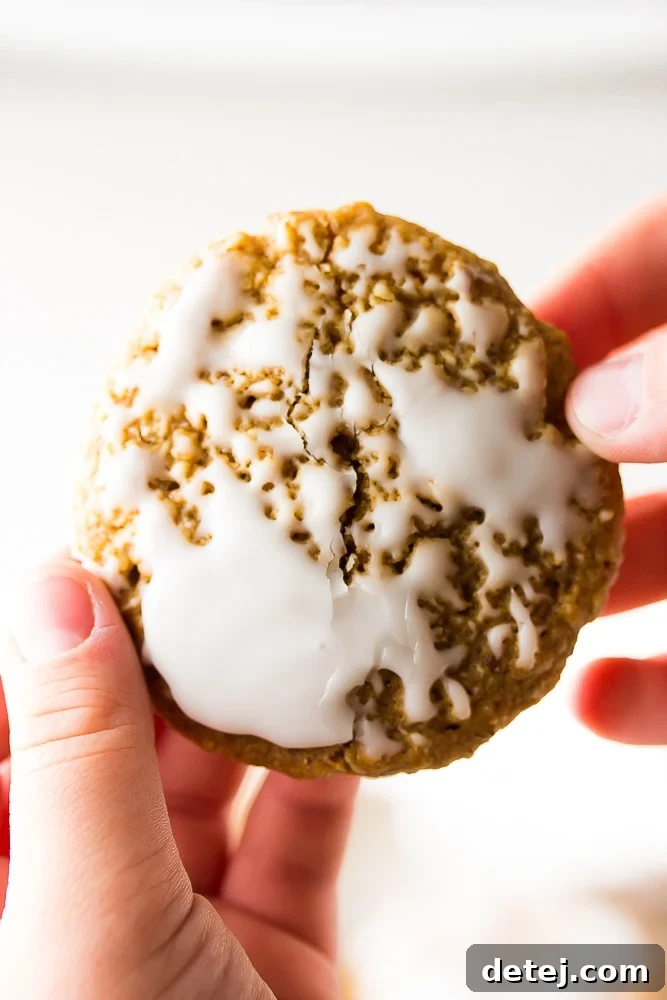 Close-up of an iced oatmeal cookie being pulled apart by hands, revealing its soft, chewy interior.