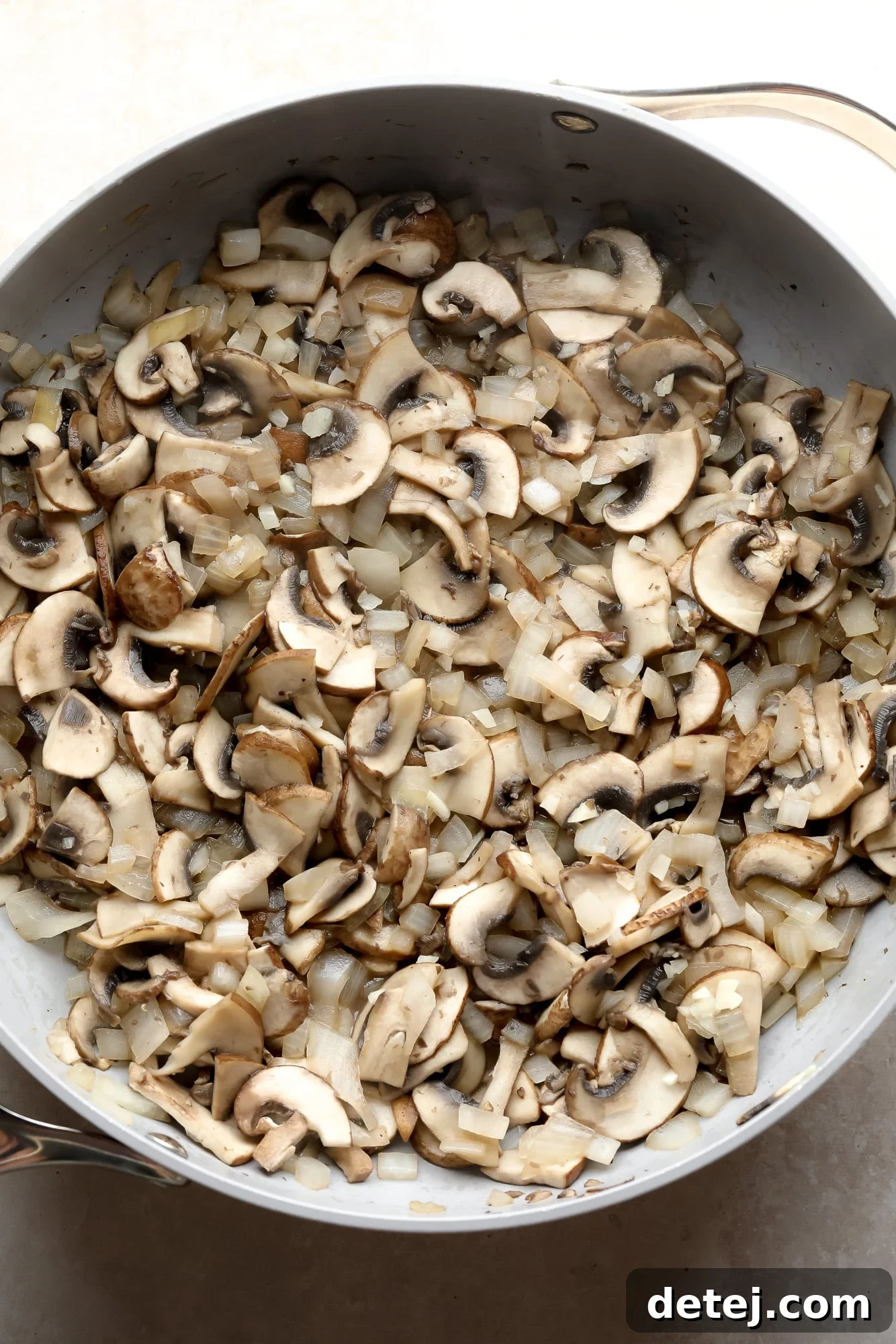 Slicing mushrooms and onions are being sautéed in a large grey pot, creating a fragrant base for the stroganoff sauce.