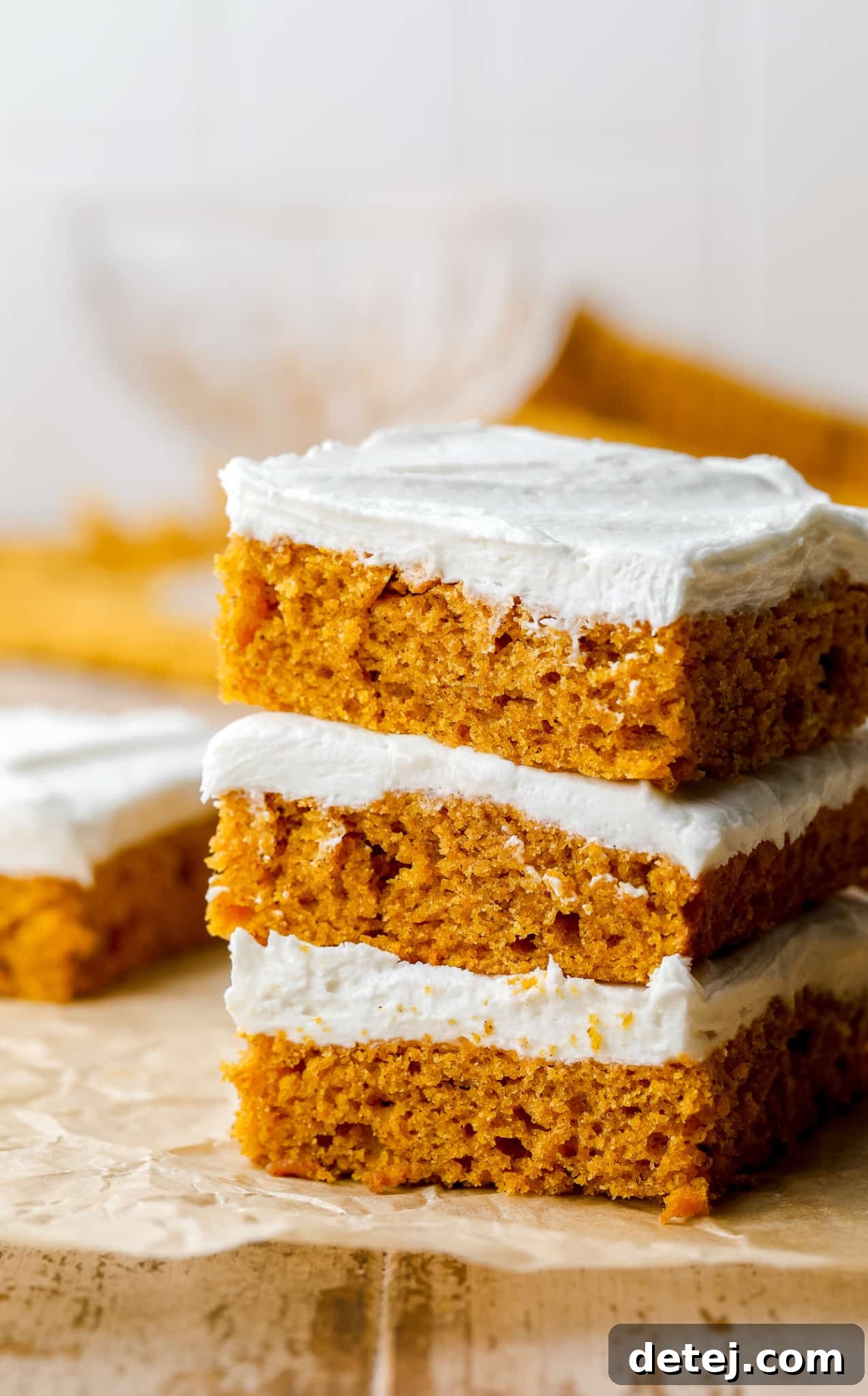 3 vegan pumpkin cake bars stacked on top of each other, showcasing their fluffy texture and creamy frosting.