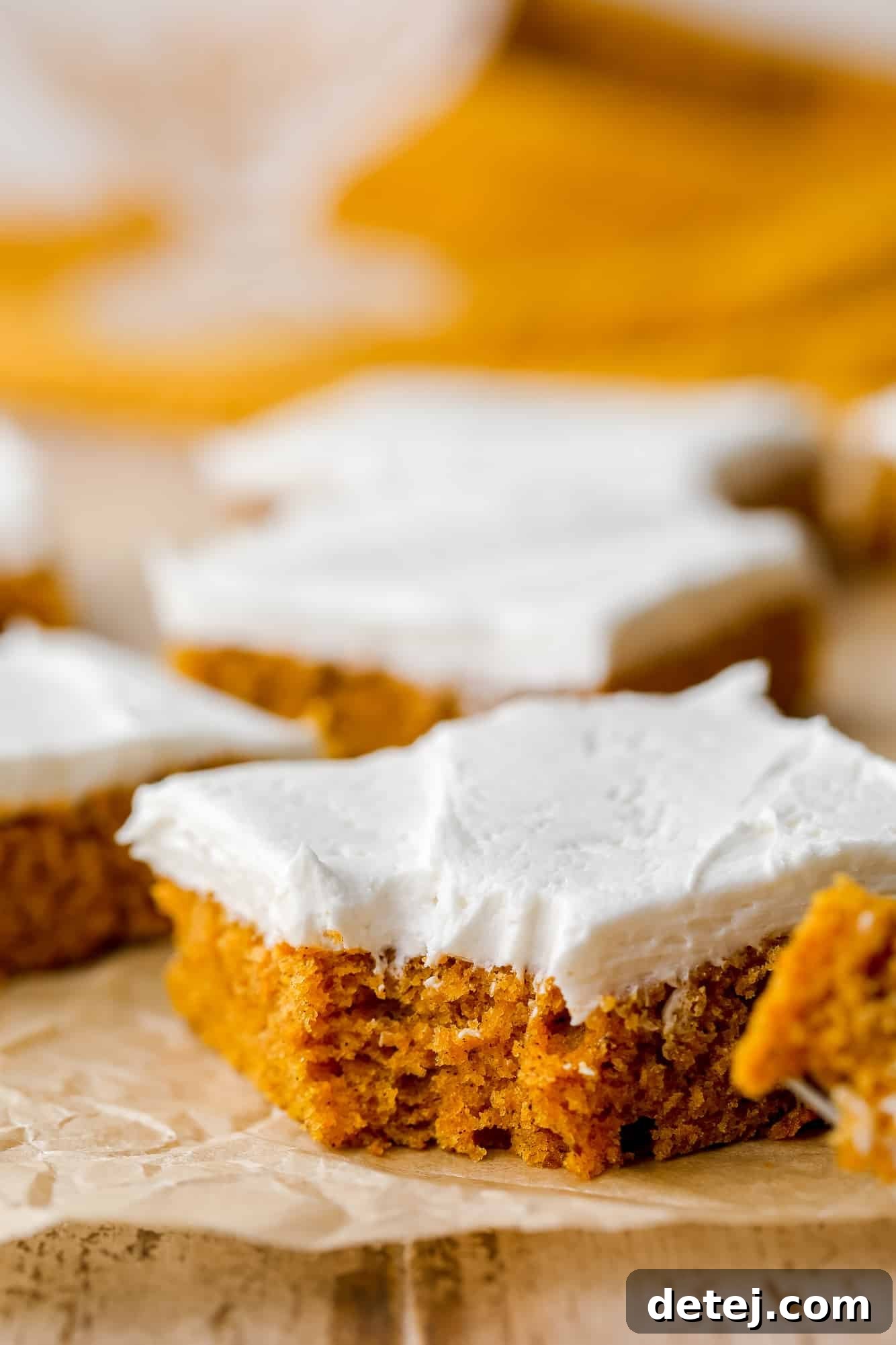 A single vegan pumpkin cake bar with a bite taken out, showing the fluffy cake and creamy frosting.