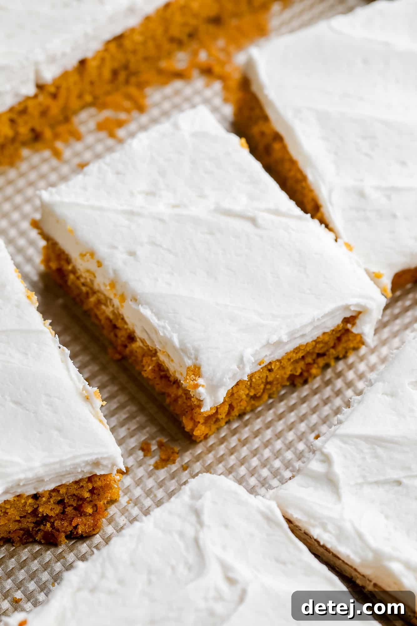Overhead view of several vegan pumpkin cake bars with generous cream cheese frosting, ready to be served.