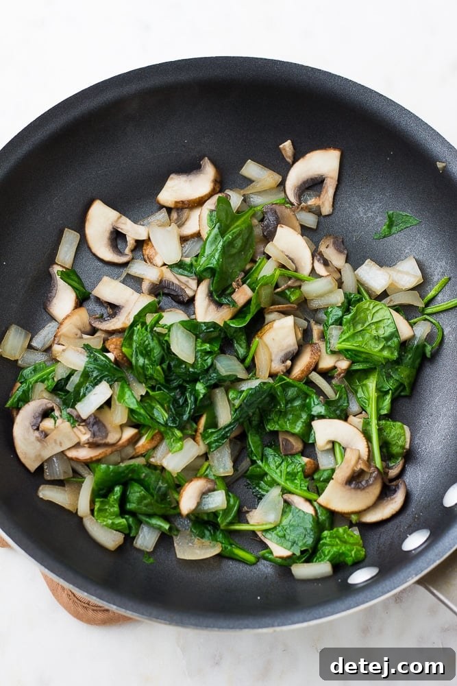 spinach and mushrooms and onions in a black pan being cooked