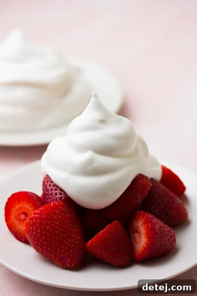 Freshly made vegan whipped cream generously dolloped on vibrant red strawberries, set against a soft pink background.