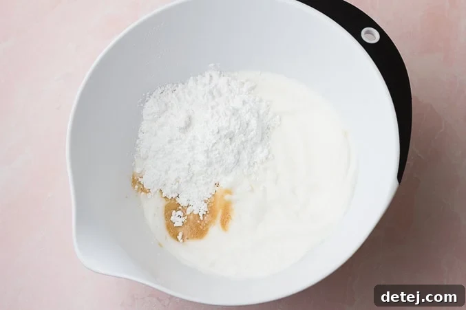 Powdered sugar and vanilla extract being added to the whipped aquafaba mixture in a bowl, ready for final mixing.