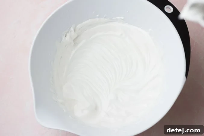 A white mixing bowl filled with perfectly whipped, fluffy white vegan whipped cream, ready to be served.