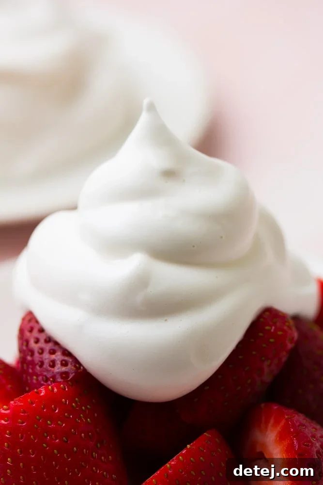A very close-up shot of fluffy vegan whipped cream artfully arranged on a plate of fresh strawberries, with a gentle pink background.