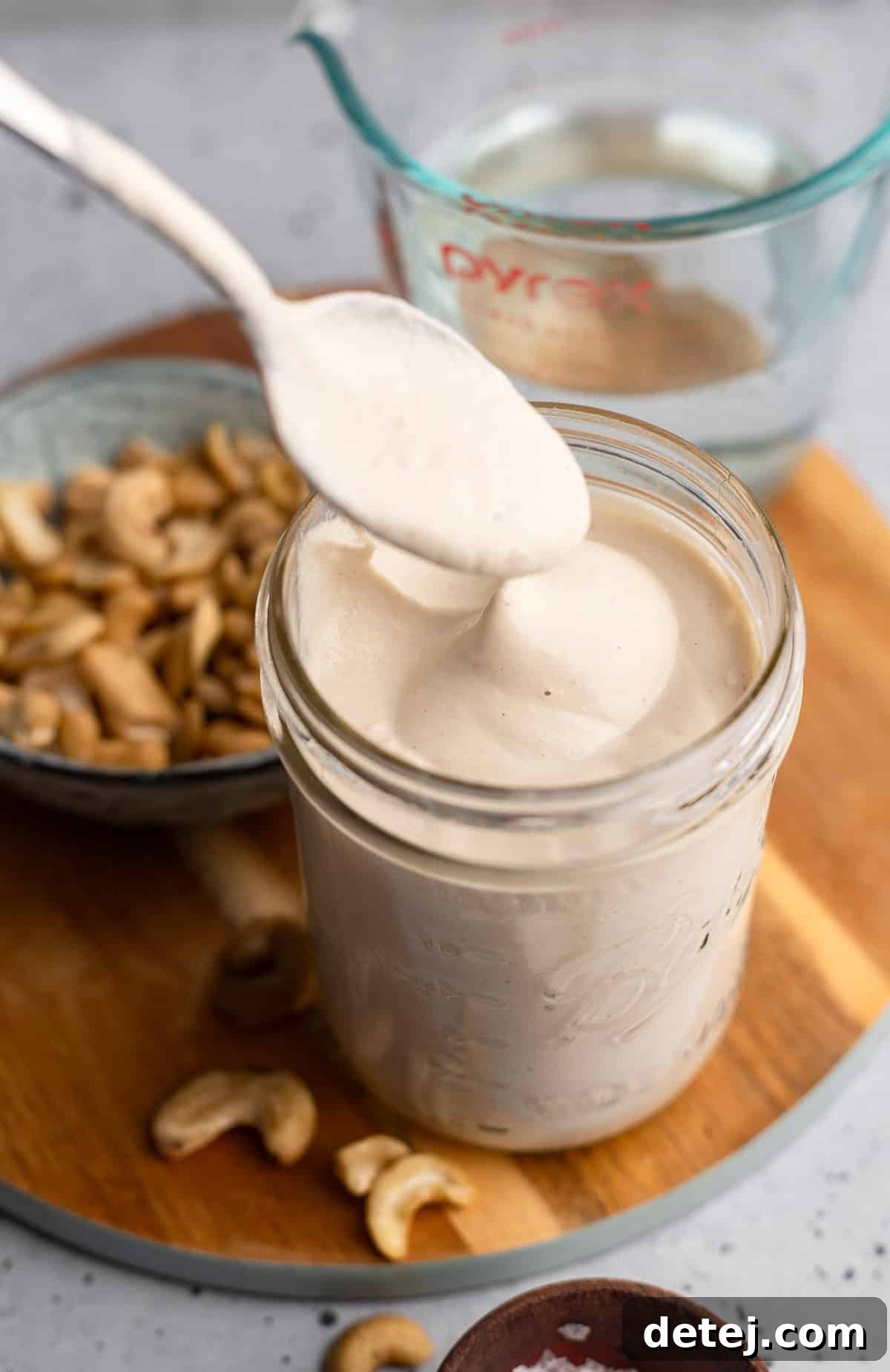 A spoon delicately lifts a generous dollop of rich cashew cream from a glass jar, showcasing its smooth, thick consistency.