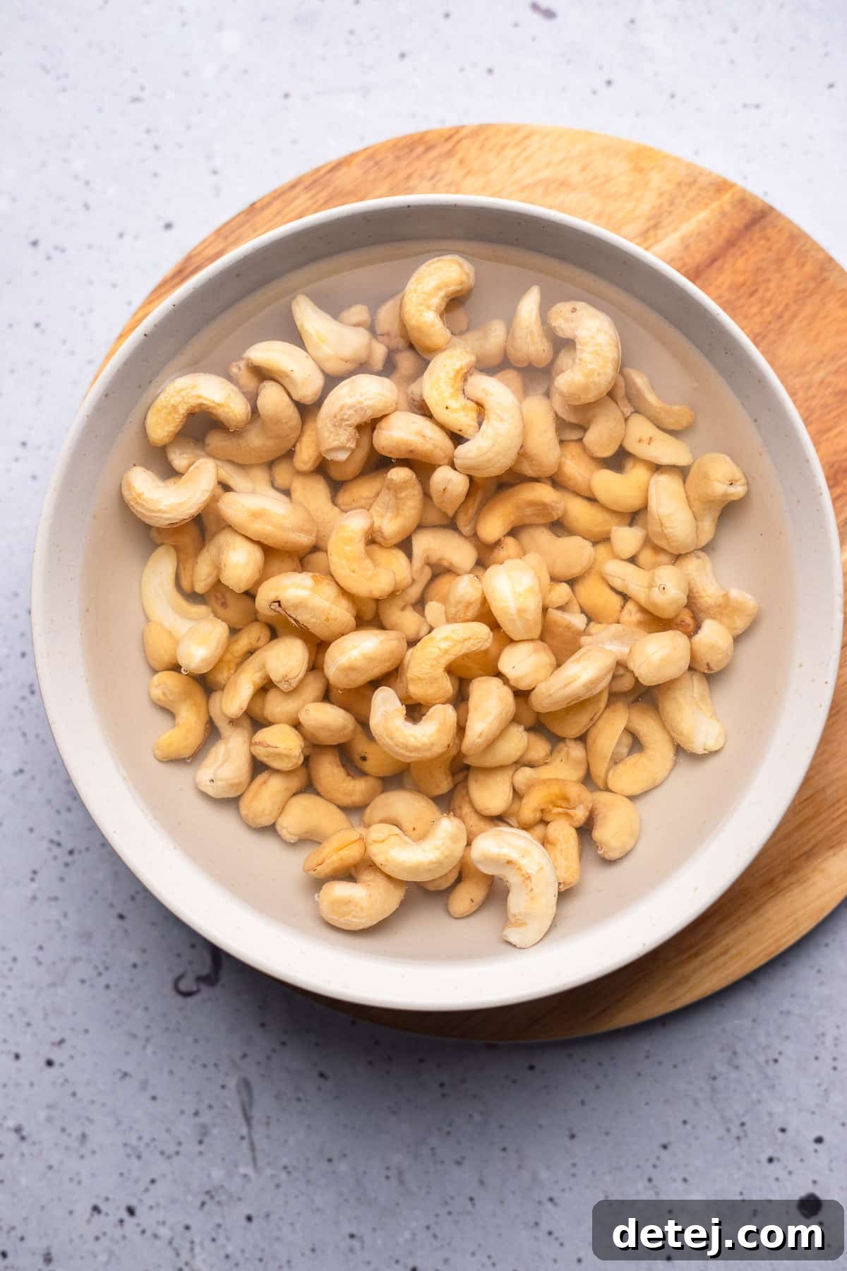 Raw cashews soaking in a bowl of hot water, softening for the blending process.