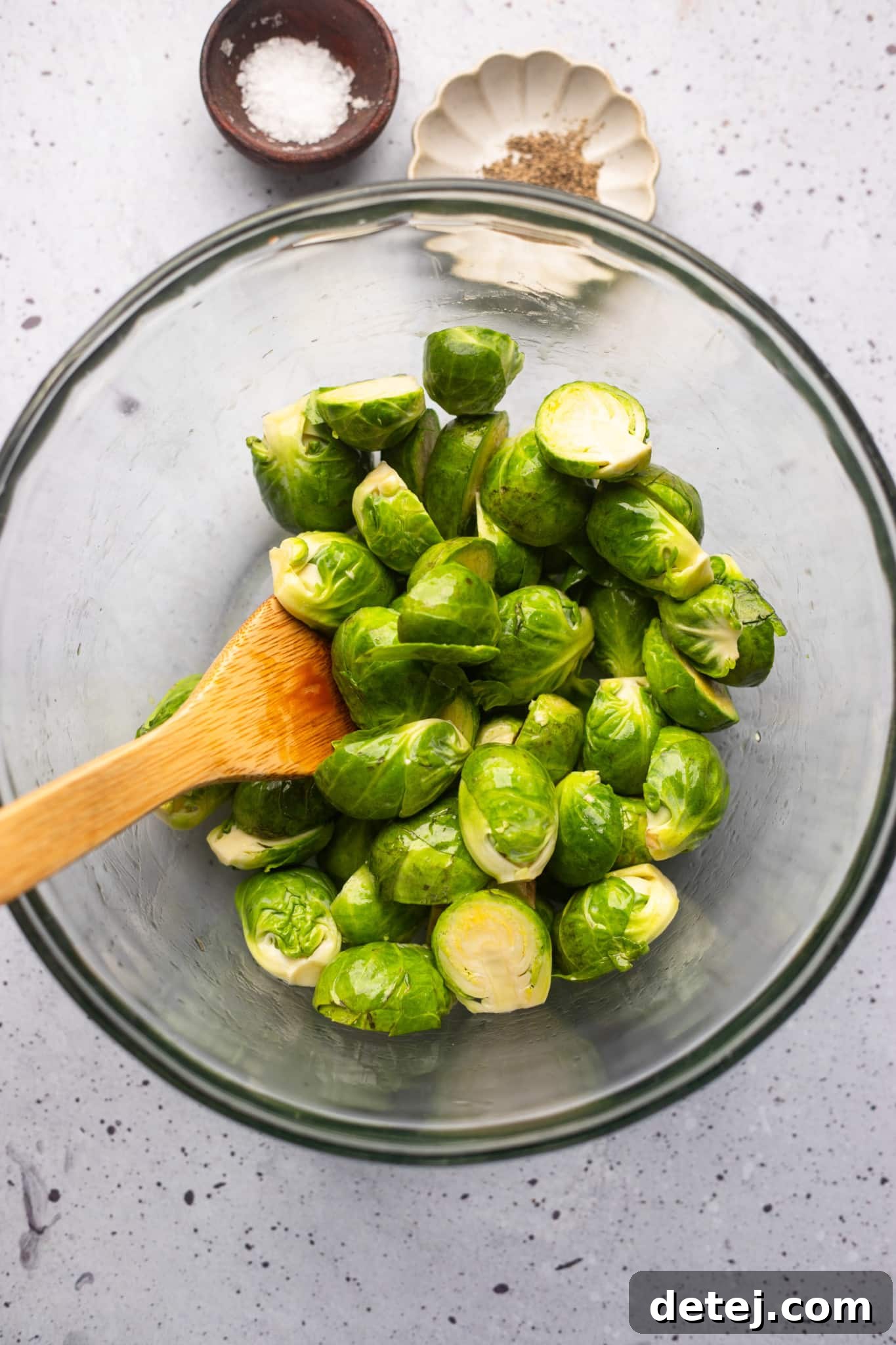 using a wooden spoon to toss brussels sprouts in oil.