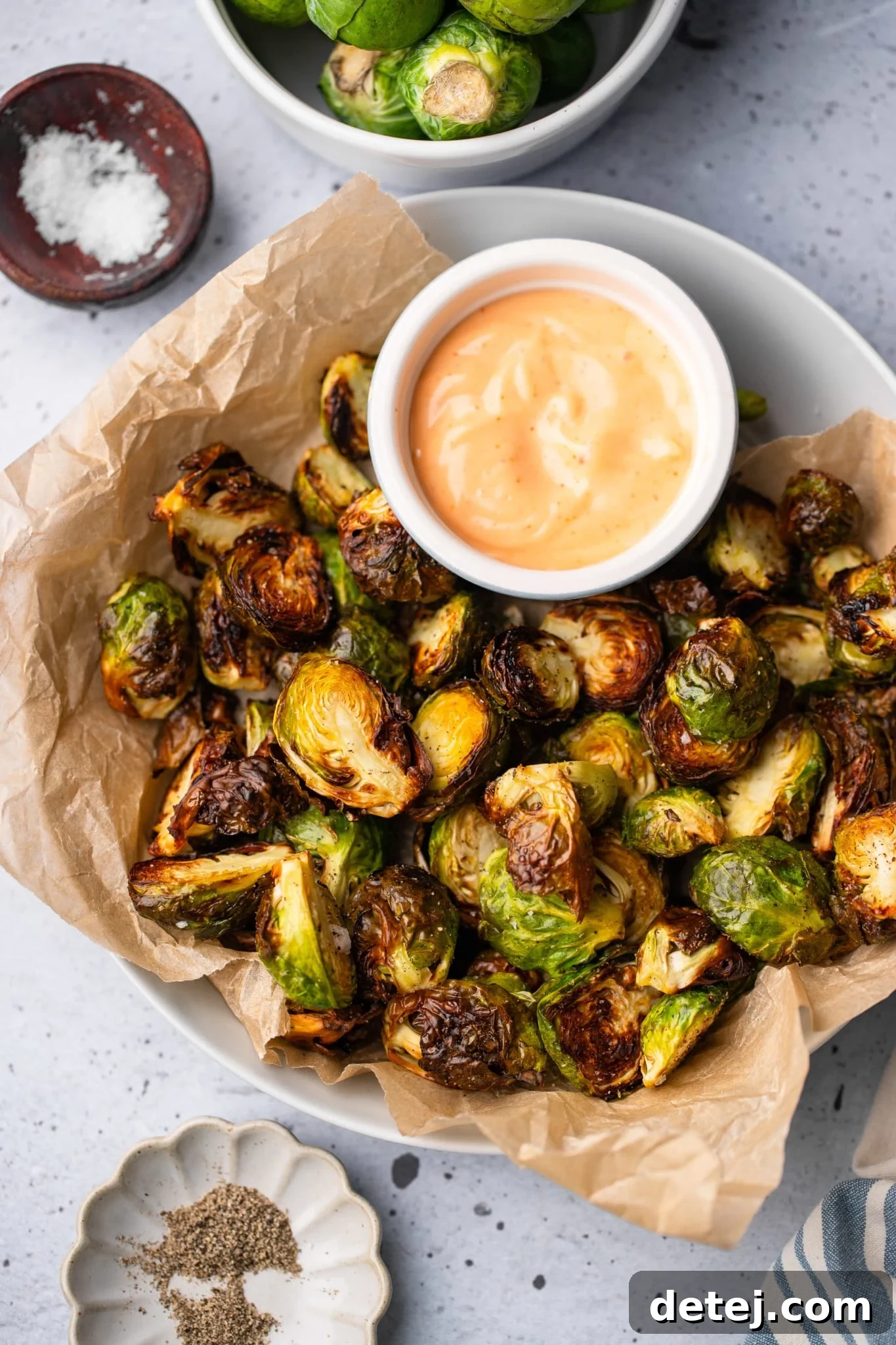 cooked brussels sprouts in a serving bowl with a small bowl of sriracha aioli on the side.