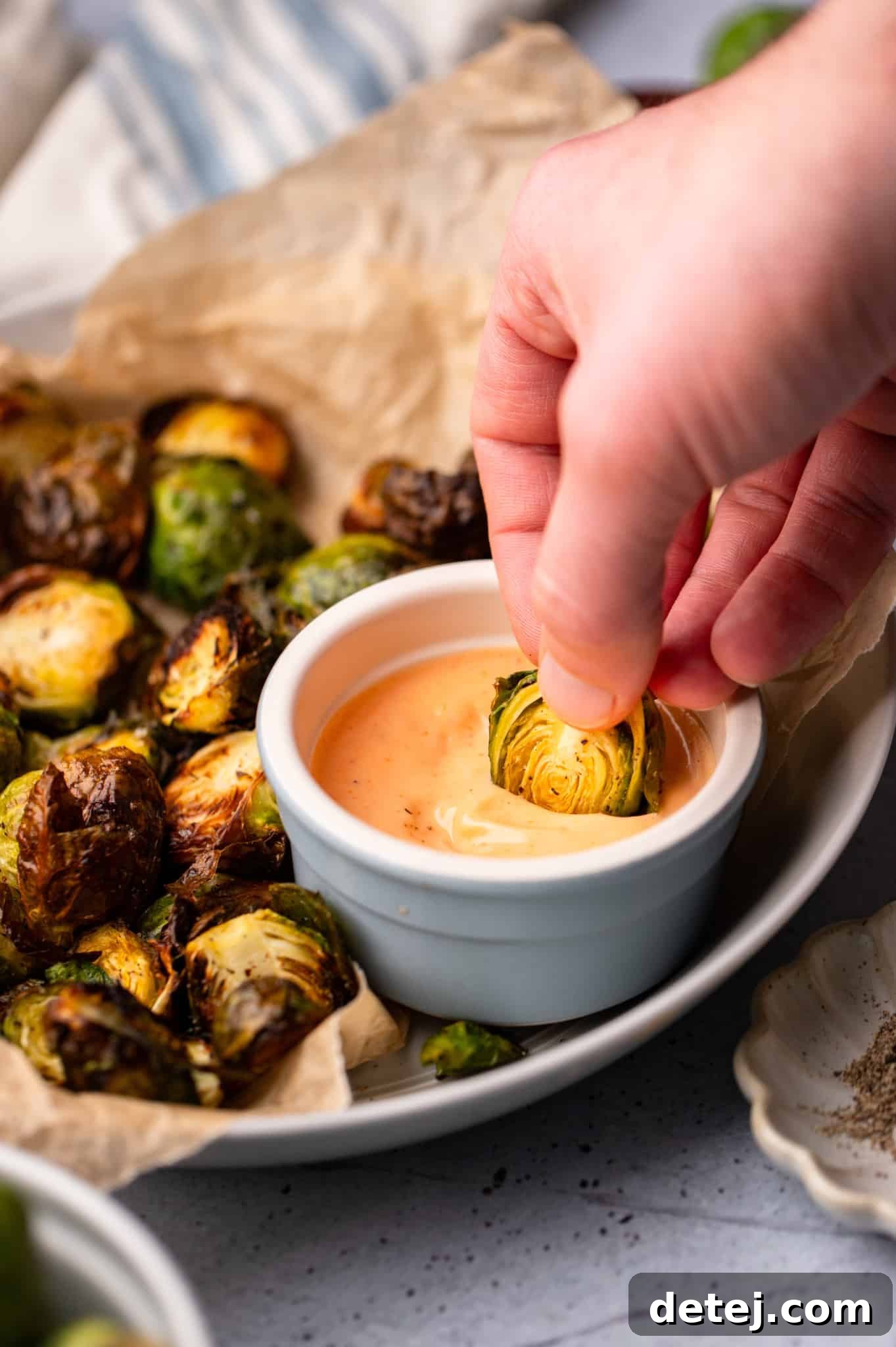 womans hand dipping a cooked brussels sprout in a bowl of chipotle aioli.