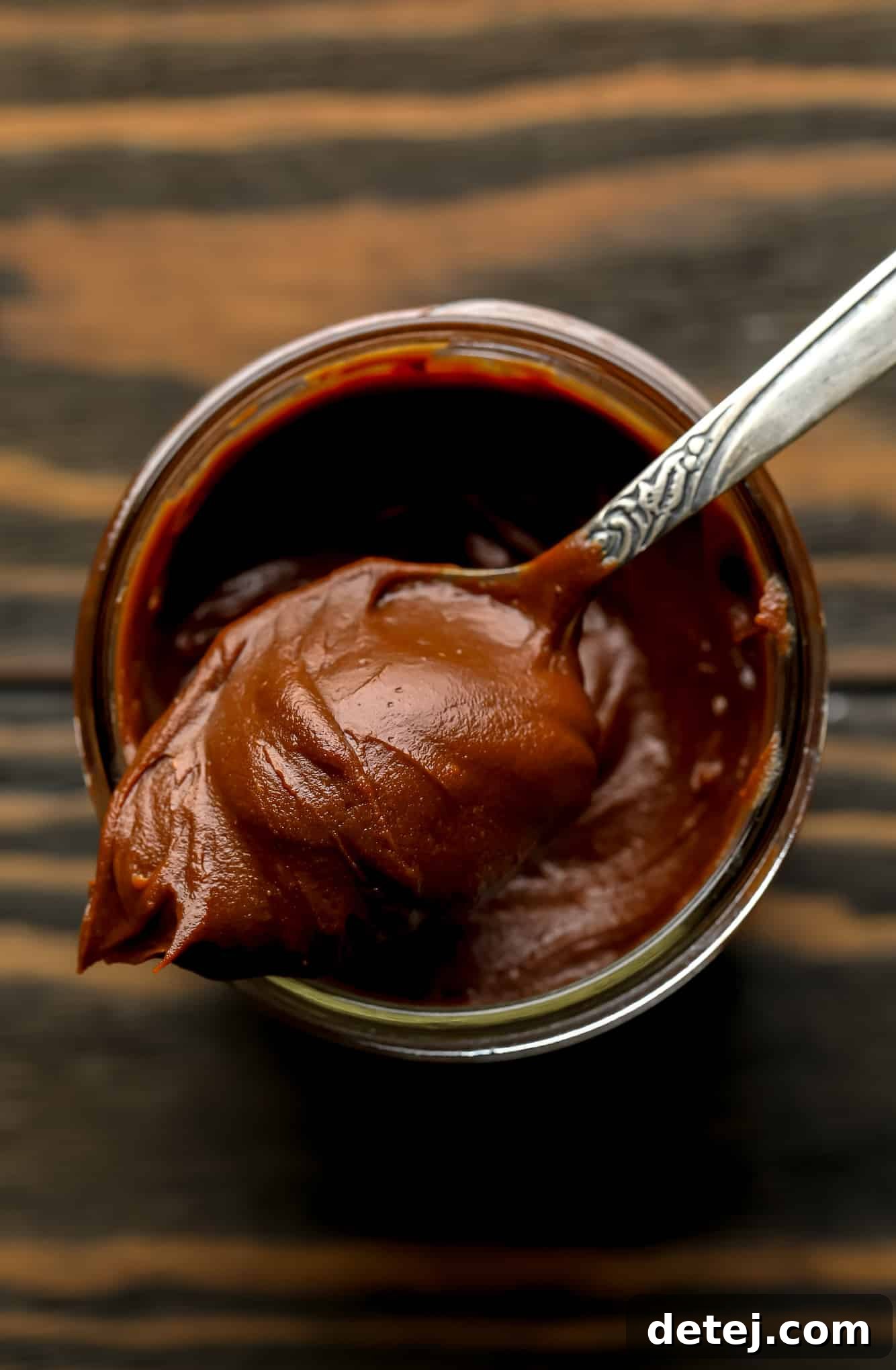 a spoon with a scoop of vegan nutella on top of a glass jar filled with more nutella.