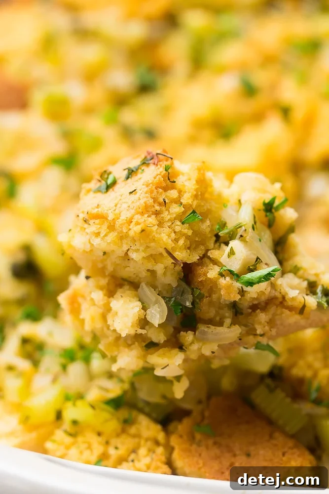 A spoonful of vegan cornbread stuffing, with the full casserole dish blurred in the background, showcasing its rich texture.