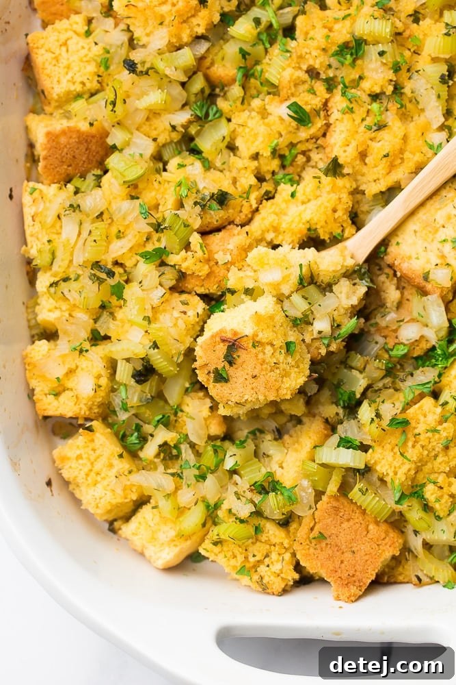 A top-down view of a golden-brown vegan cornbread stuffing casserole with a wooden spoon nestled in it, ready to be served.