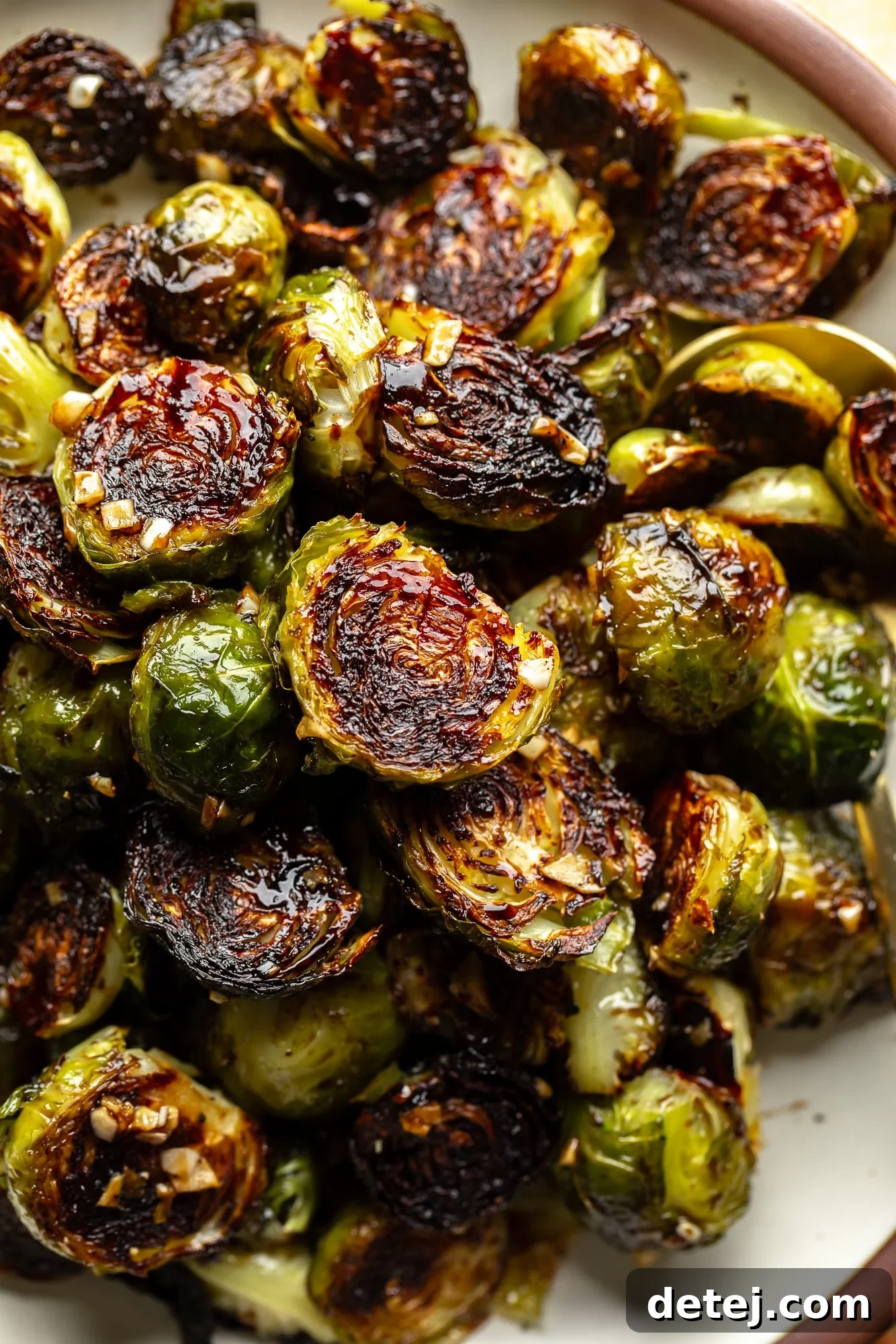 Close up on a pile of roasted Brussels sprouts with lightly charred edges, glistening with balsamic vinegar. The leaves are golden and crisp, while the insides remain tender.
