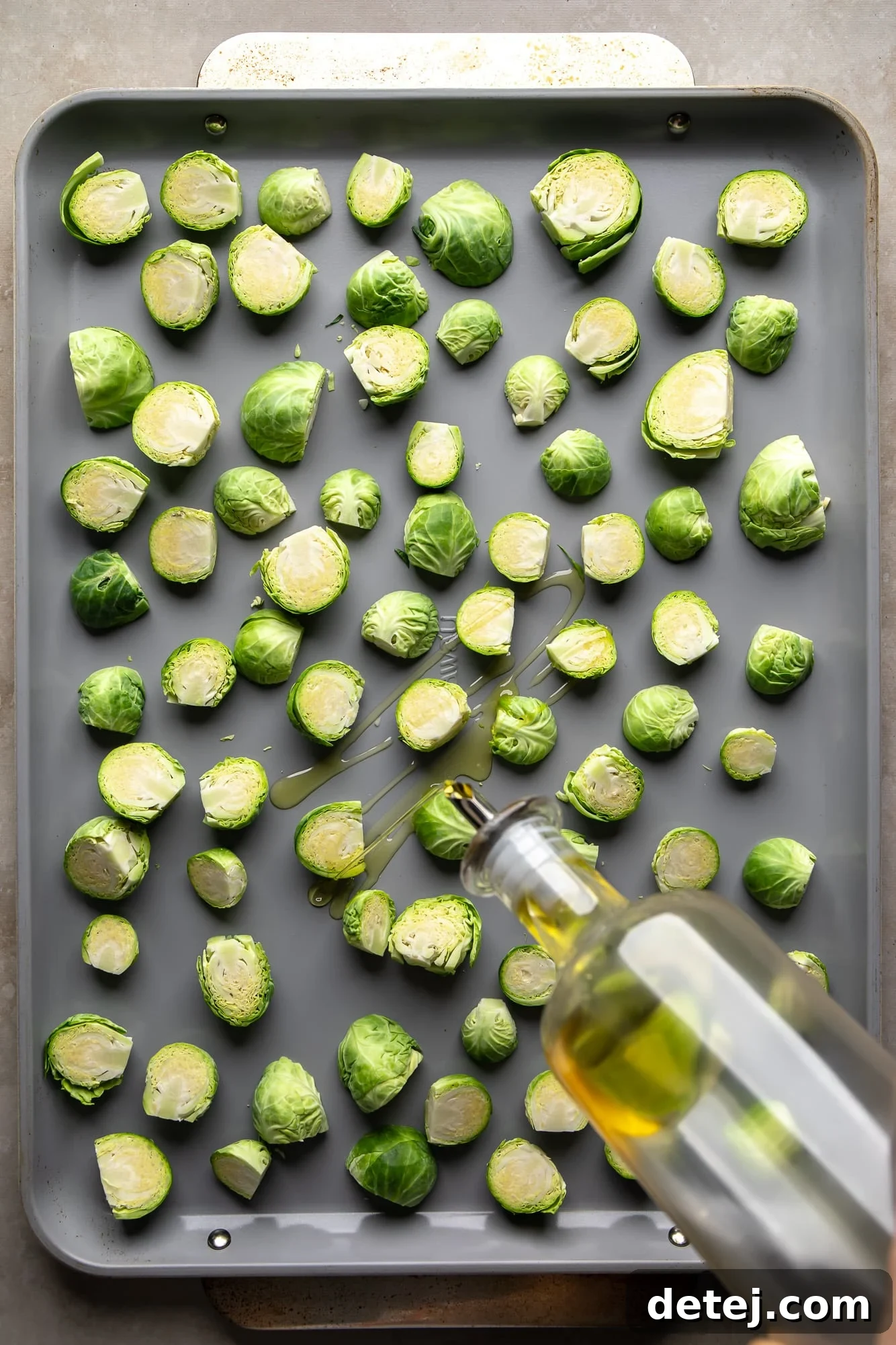 Drizzling olive oil over freshly chopped Brussels sprouts on a sheet pan, ready for seasoning.