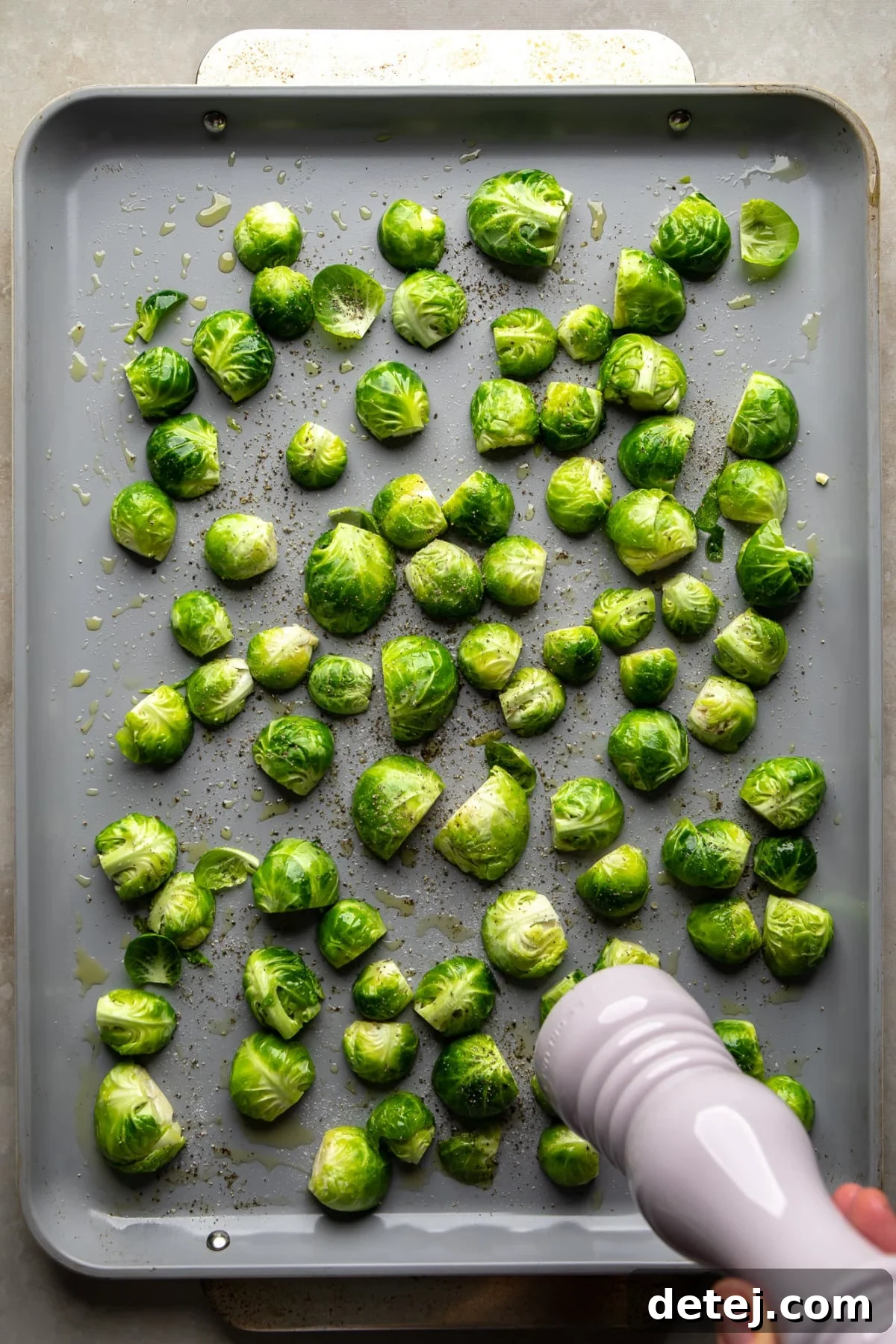 Brussels sprouts on a baking sheet, seasoned with salt and freshly ground black pepper, demonstrating thorough coating.
