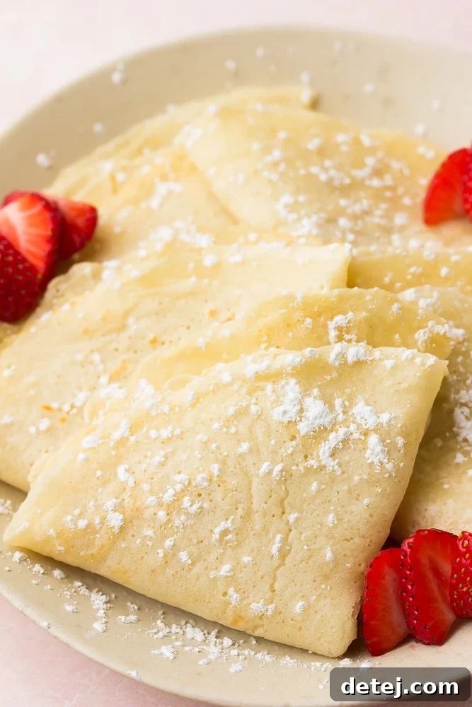 folded vegan crepes on a plate with powdered sugar and strawberries