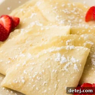 folded vegan crepes on a plate with powdered sugar and strawberries