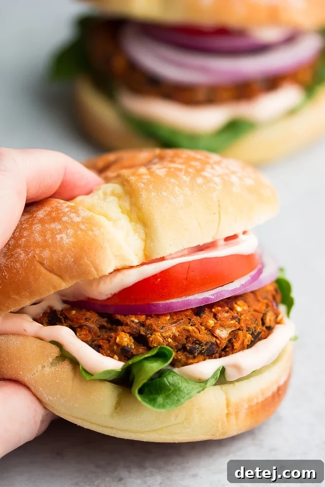 Hand grabbing a perfectly cooked sweet potato black bean burger on a bun with fresh toppings, showcasing its delicious texture and vibrant colors.